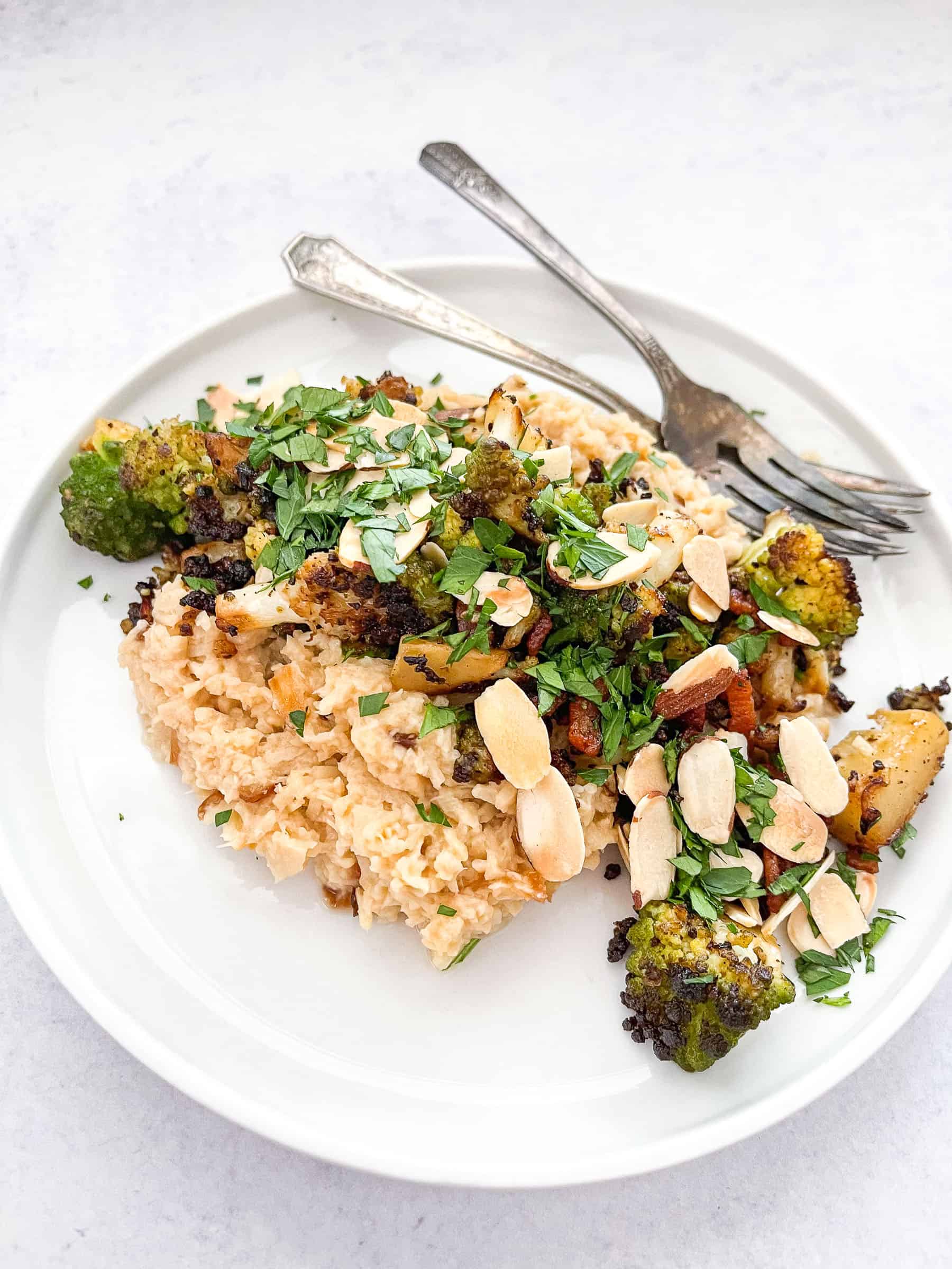 keto risotto with romanesco and bacon on a white plate with two forks and a white background