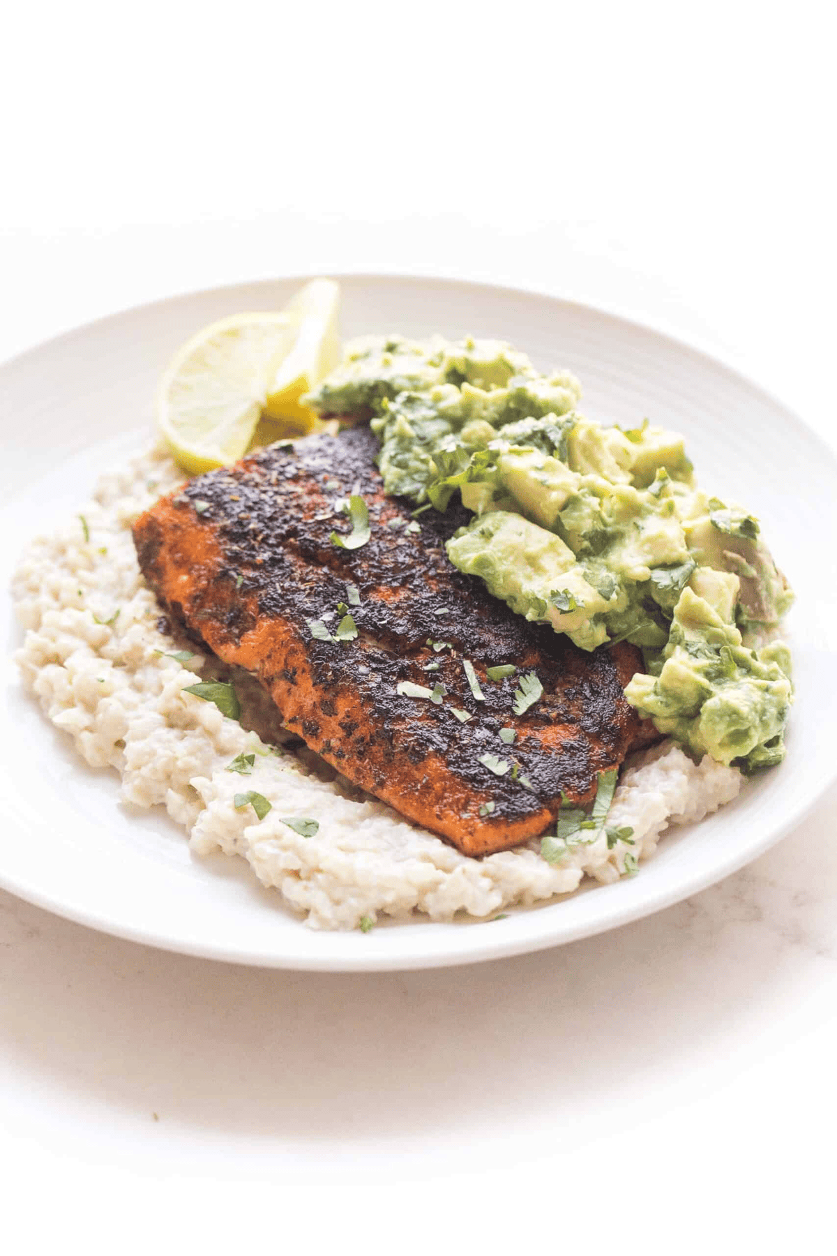 a white plate topped with cauliflower rice, salmon, chunky guacamole, and slices of lemons