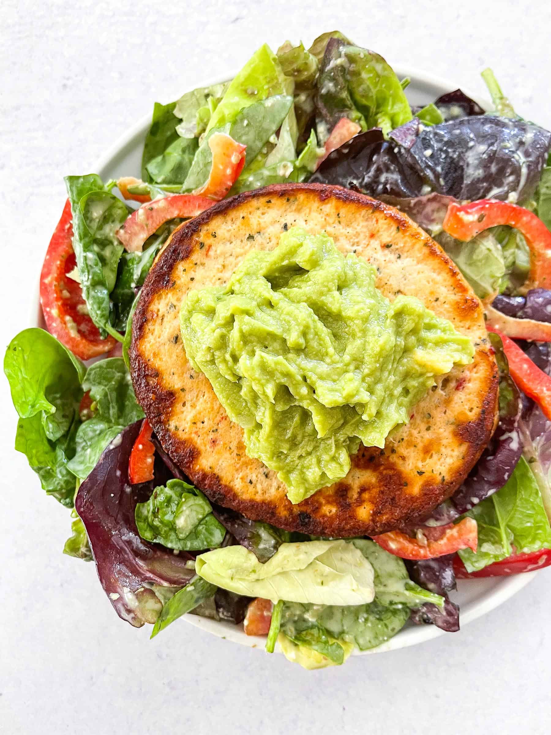 chile lime chicken burger patty on a bed of lettuce with red bell pepper and guacamole in a white bowl and a white background
