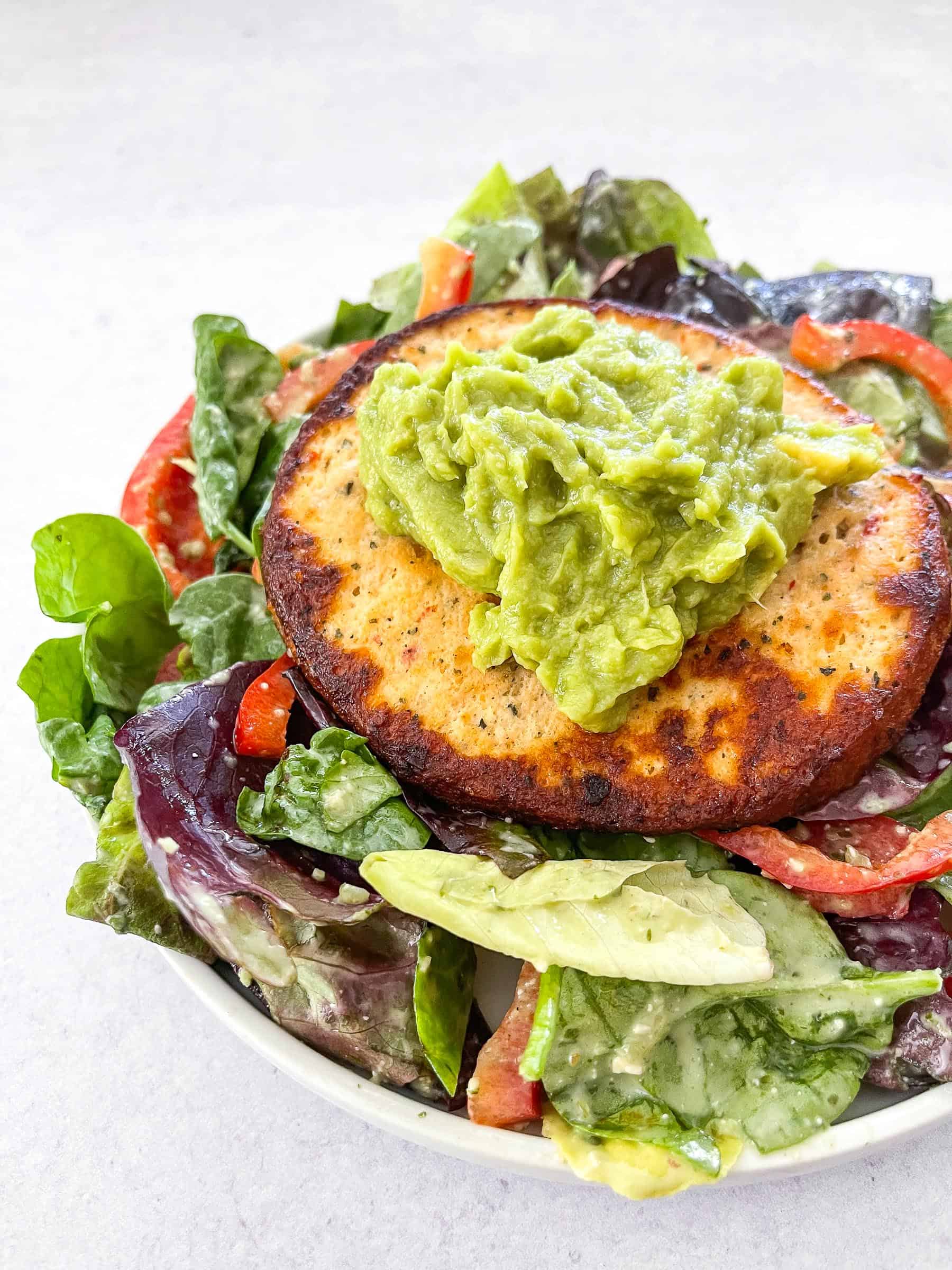 chile lime chicken burger patty on a bed of lettuce with red bell pepper and guacamole in a white bowl and a white background