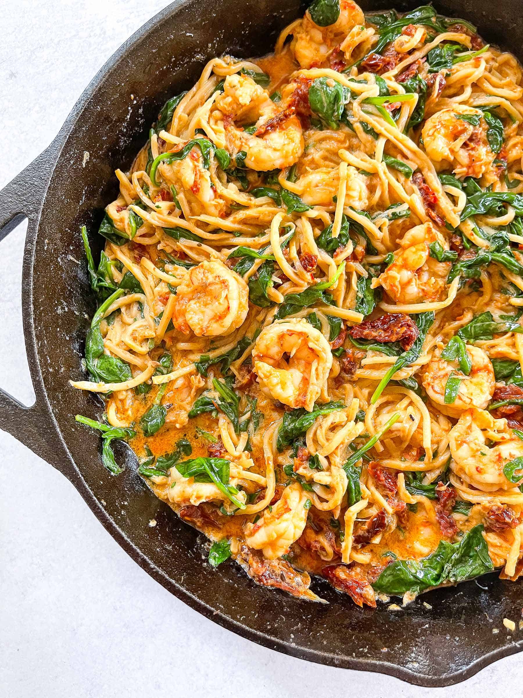 keto creamy tuscan shrimp pasta topped with basil in a cast iron skillet with a white background