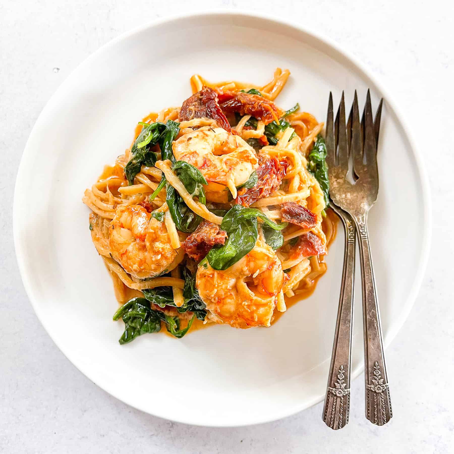 keto creamy tuscan shrimp pasta topped with basil on a white plate with two forks and a white background