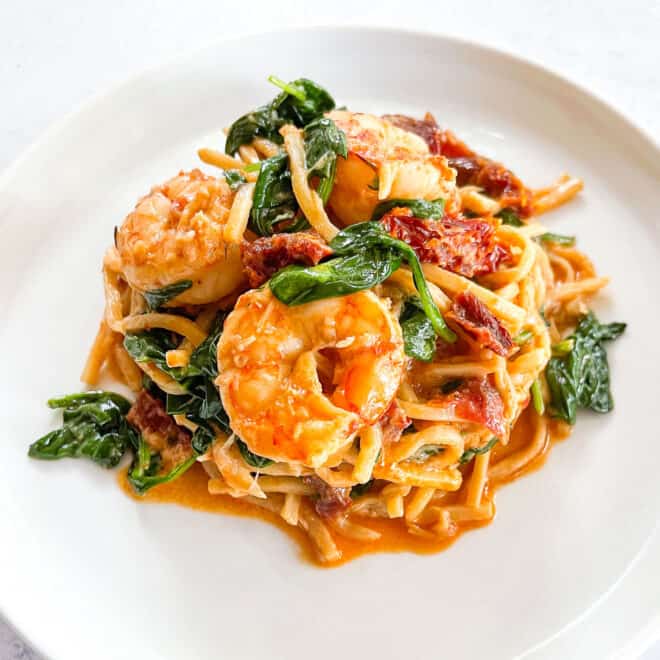 keto creamy tuscan shrimp pasta topped with basil on a white plate with a white background