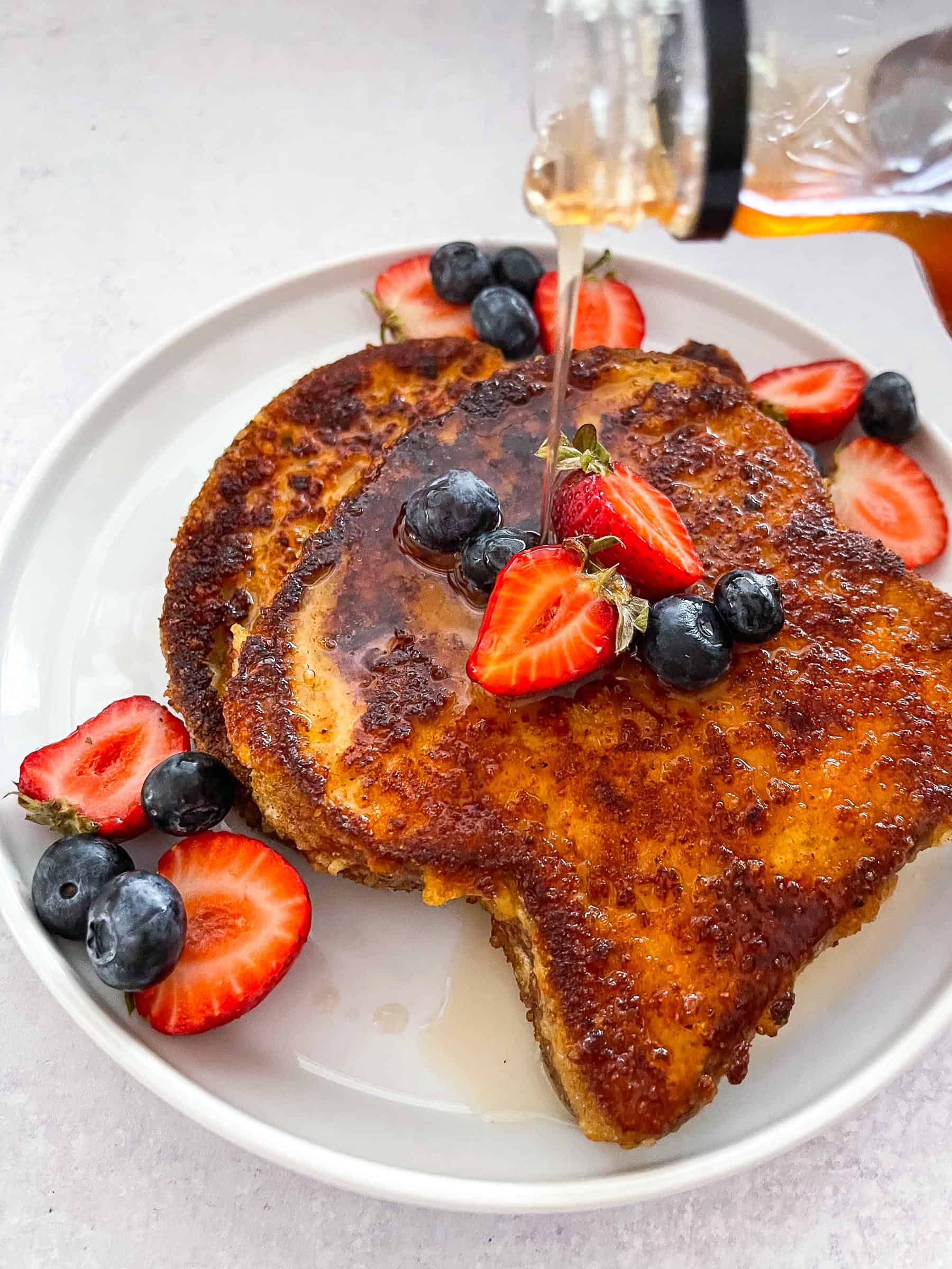 keto crusted french toast topped with syrup, blueberries, and strawberries on a white plate with a white background