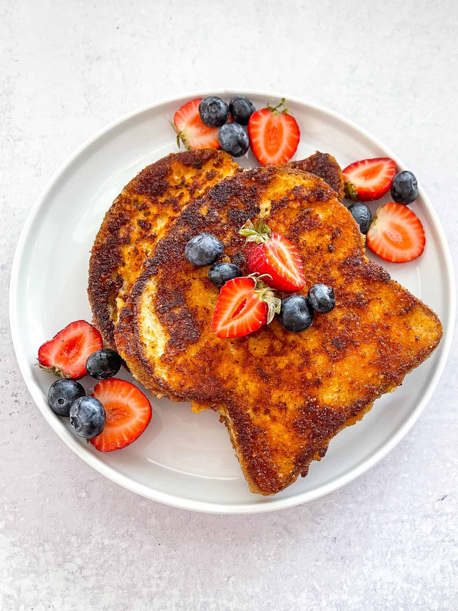 keto crusted french toast topped with syrup, blueberries, and strawberries on a white plate with a white background