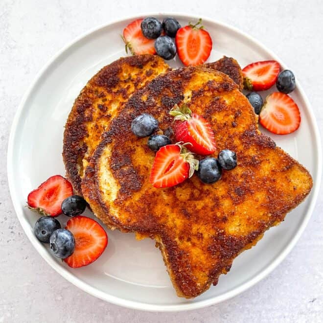 keto crusted french toast topped with syrup, blueberries, and strawberries on a white plate with a white background