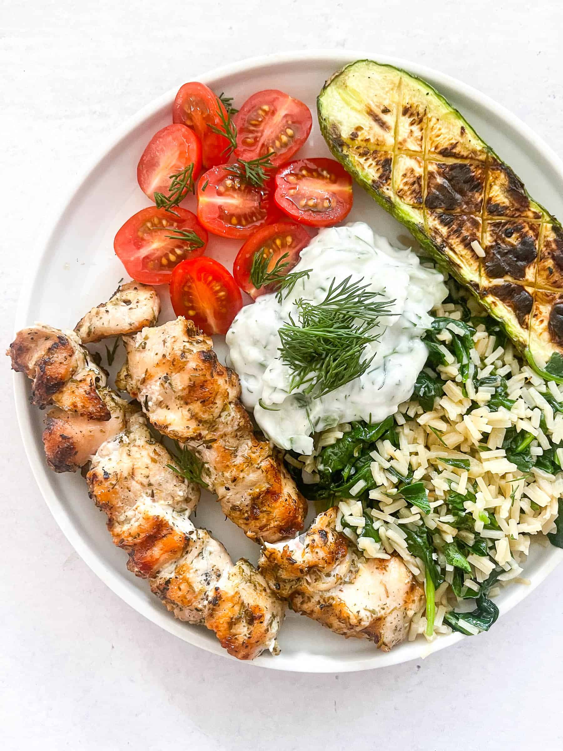 keto grilled chicken kabobs on a white plate with veggies and tzatziki sauce with a white background