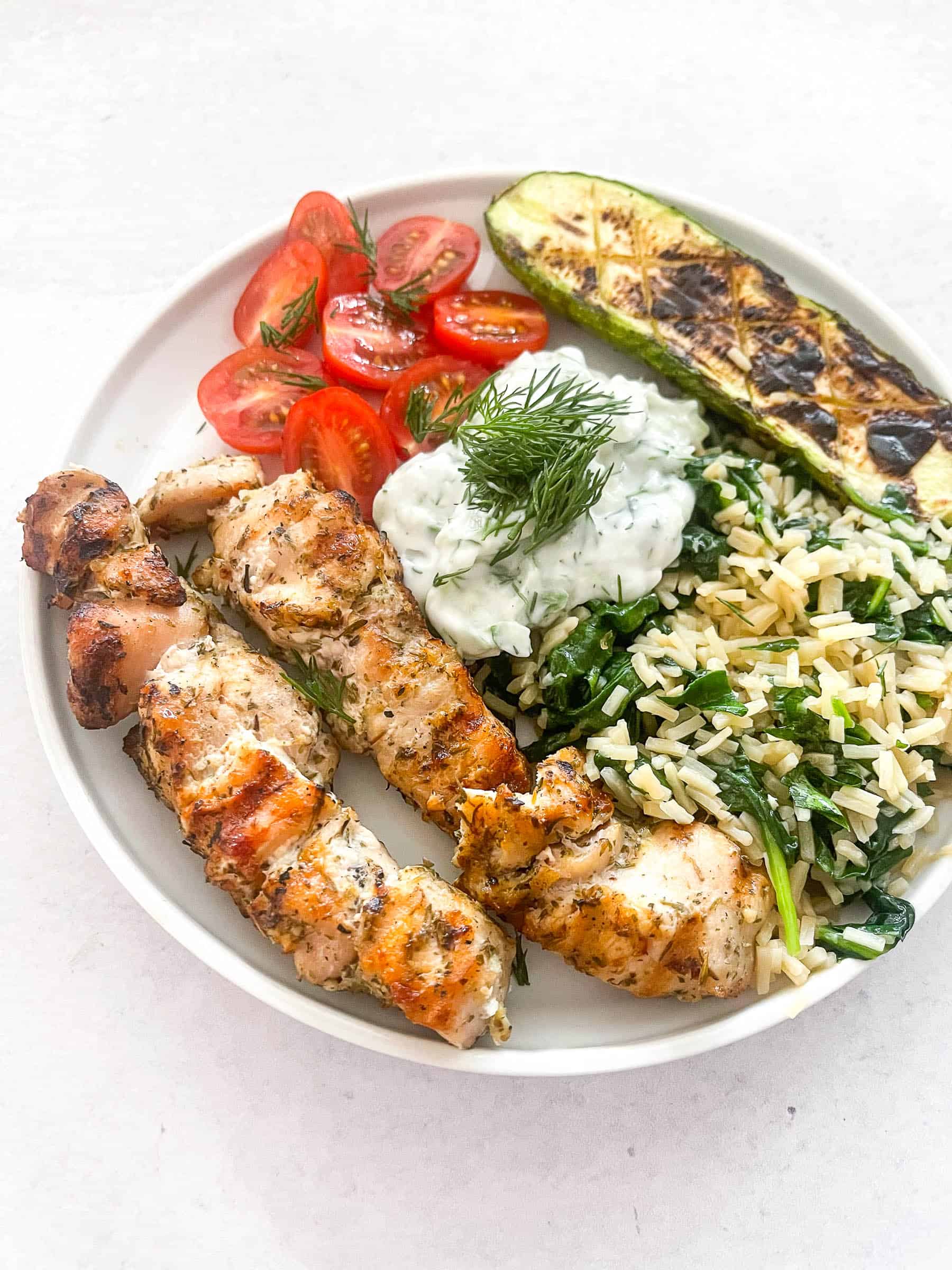 keto grilled chicken kabobs on a white plate with veggies and tzatziki sauce with a white background