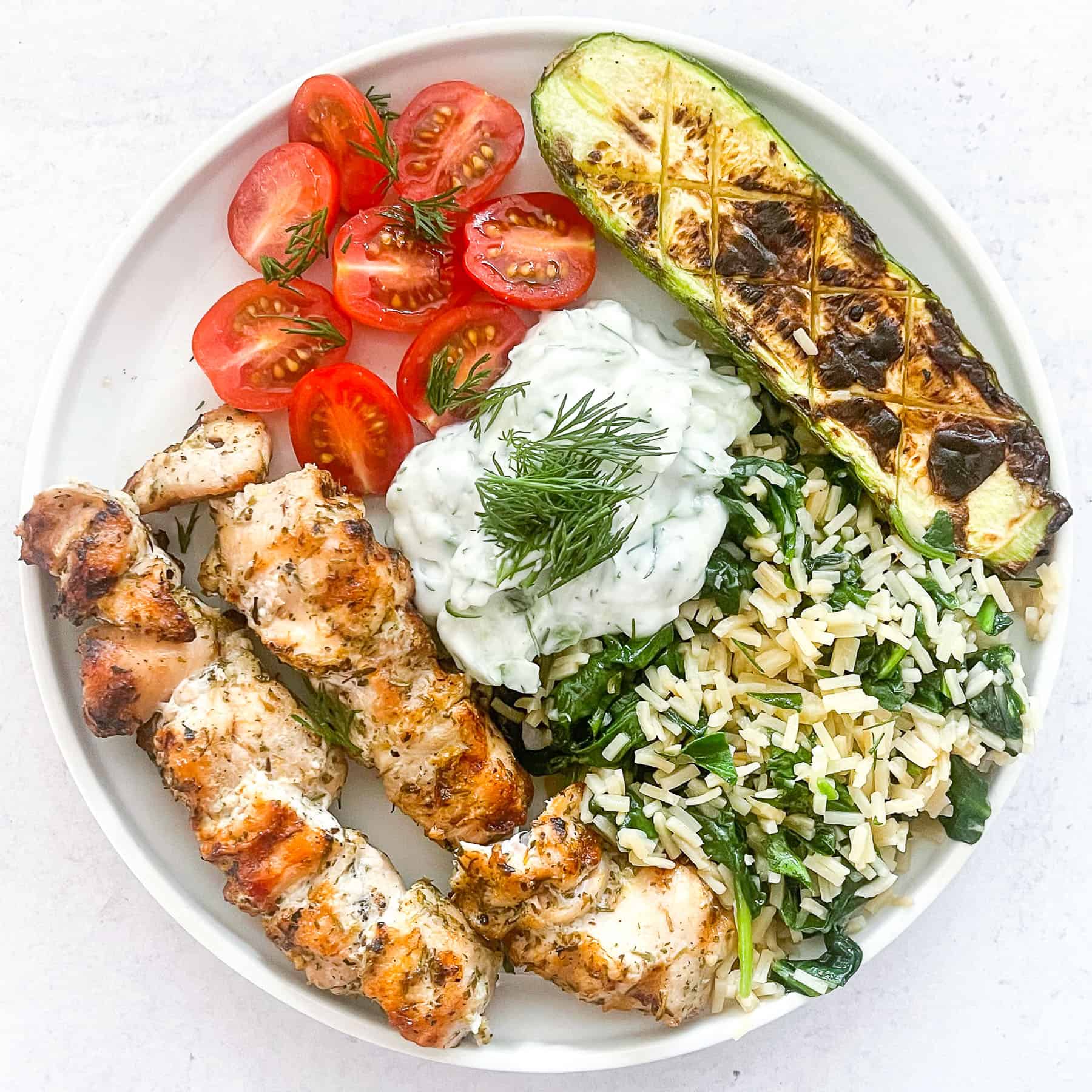 keto grilled chicken kabobs on a white plate with veggies and tzatziki sauce with a white background
