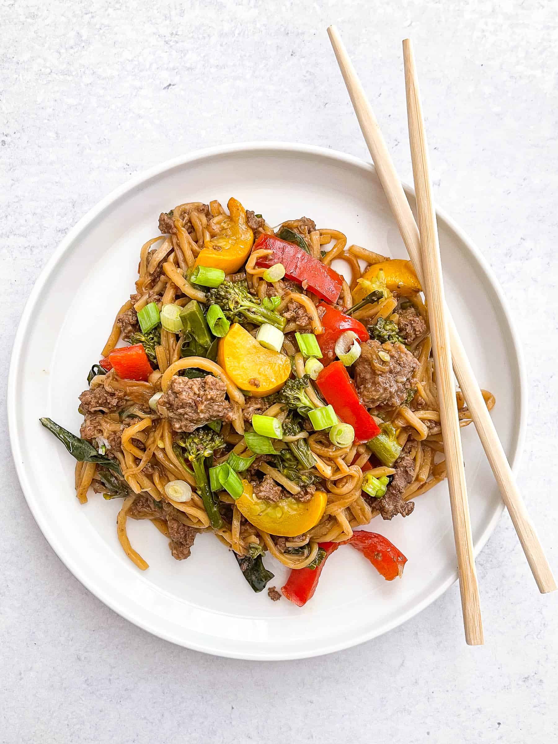 keto beef and vegetable noodle stir fry on a white plate with two chopsticks and a white background