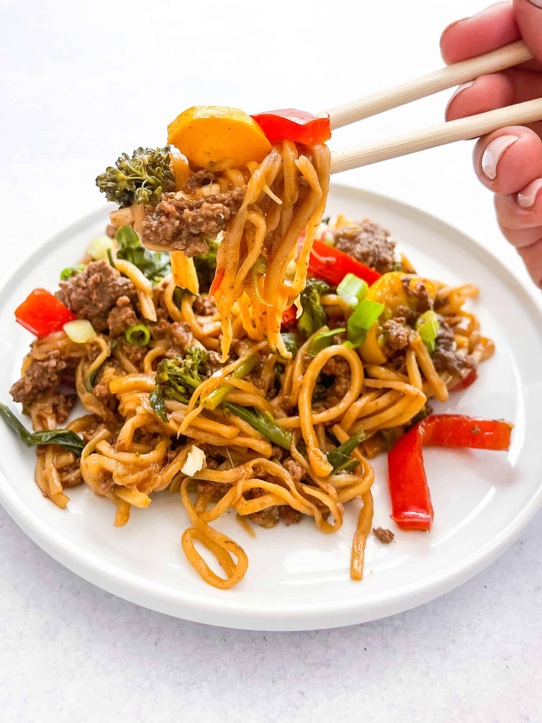 keto beef and vegetable noodle stir fry on a white plate with two chopsticks holding the stir fry with a white background