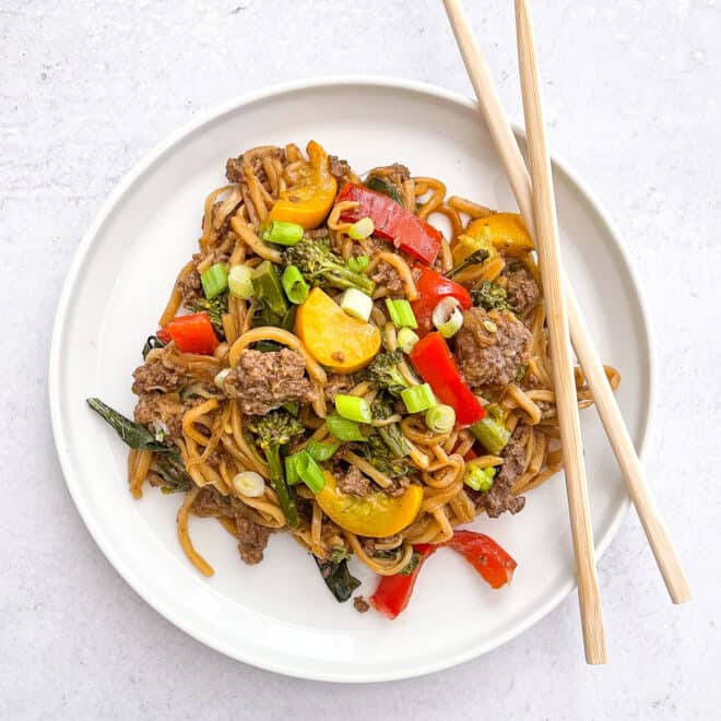 keto beef and vegetable noodle stir fry on a white plate with two chopsticks and a white background