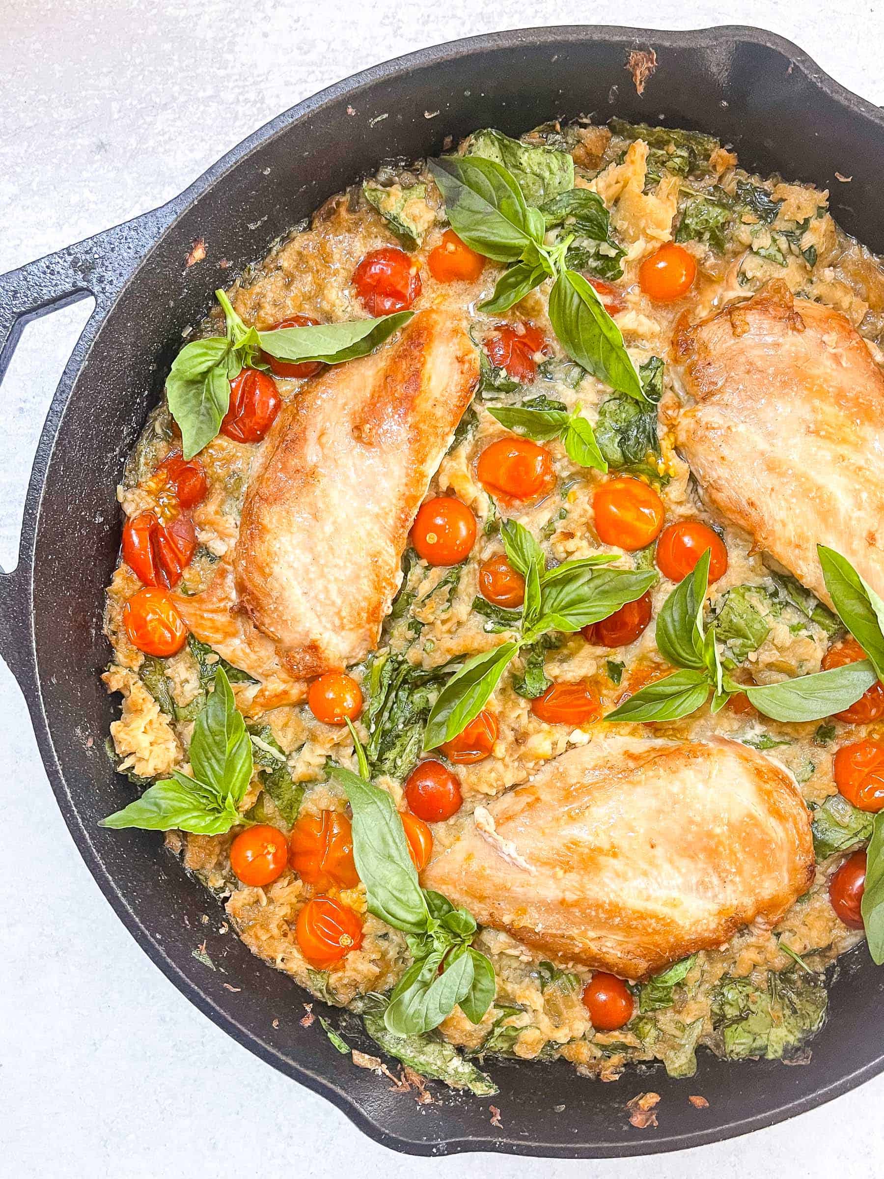 keto creamy chicken and tomato casserole in a black cast iron skillet with a white background