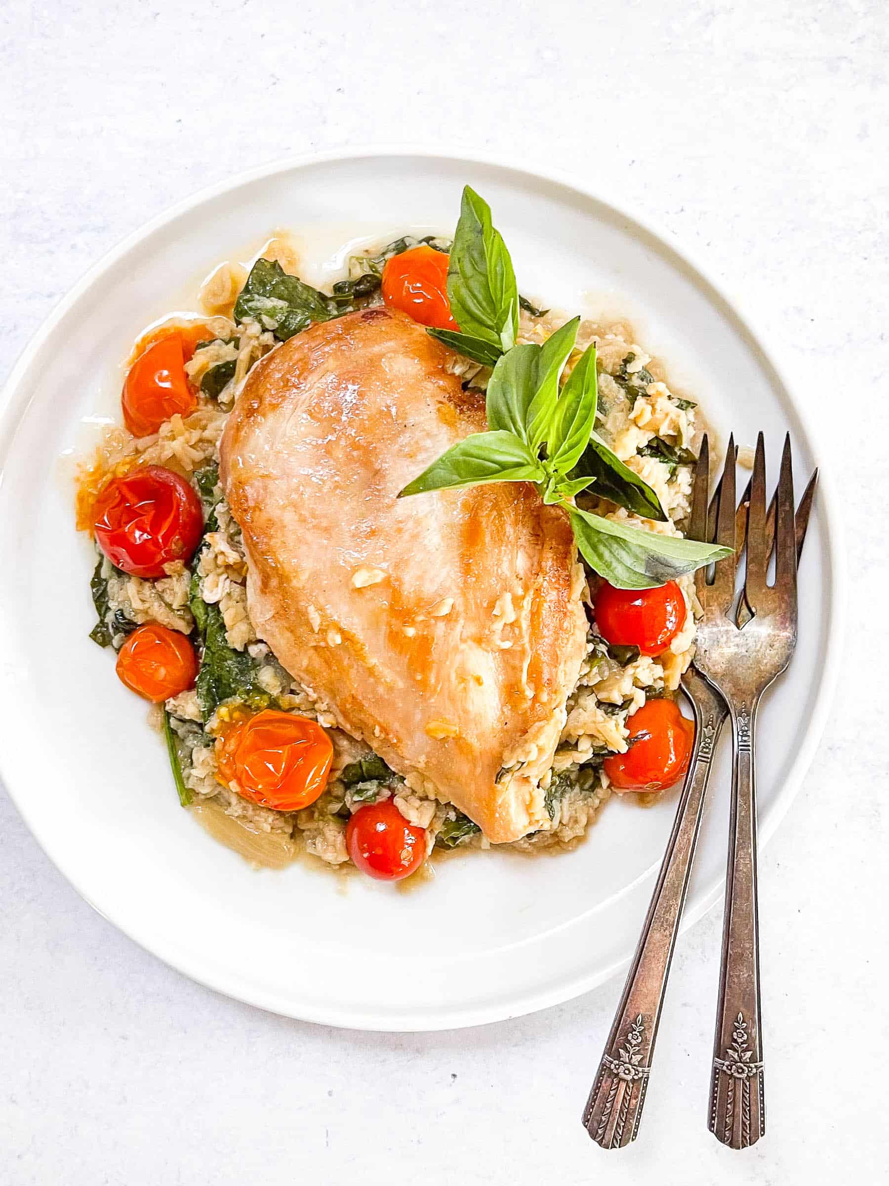 keto creamy chicken and tomato casserole on a white plate with two antique forks and a white background