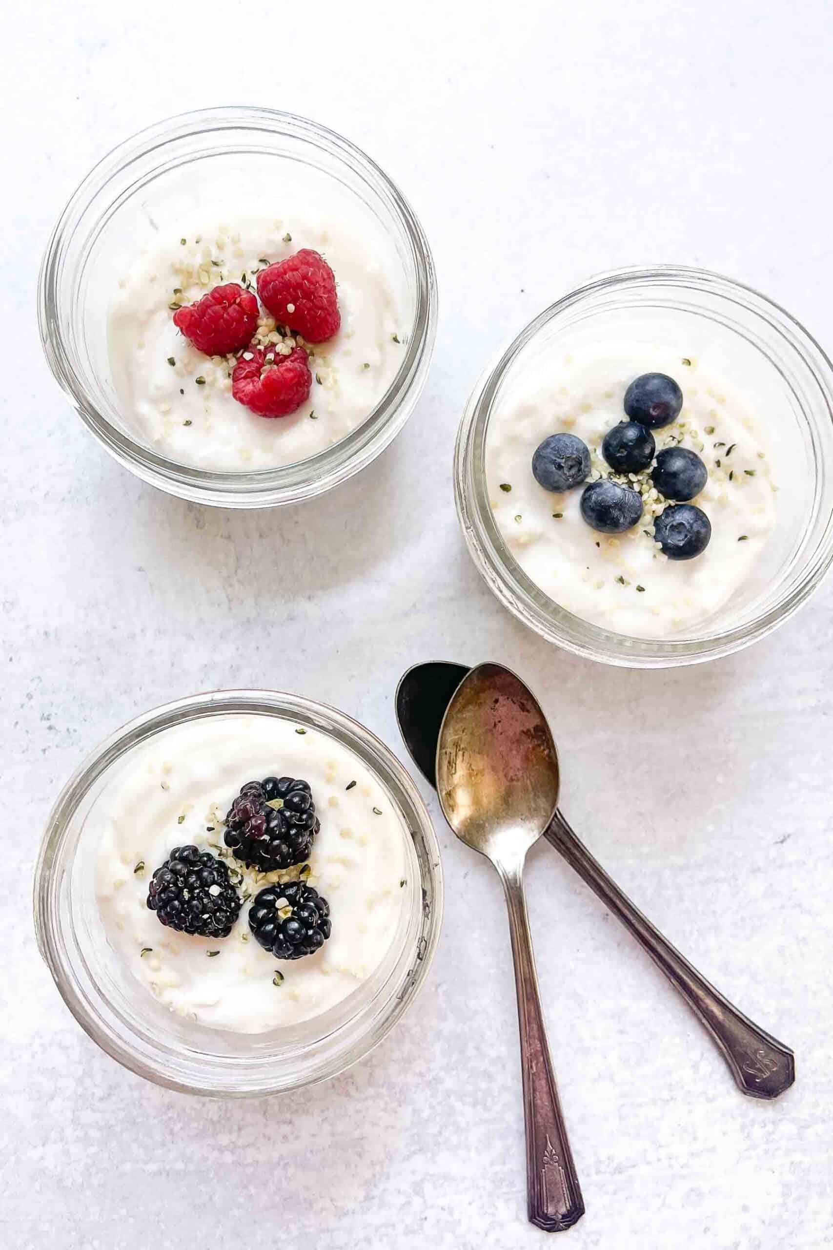 three small glass jars of coconut yogurt each topped with a different berry and seeds
