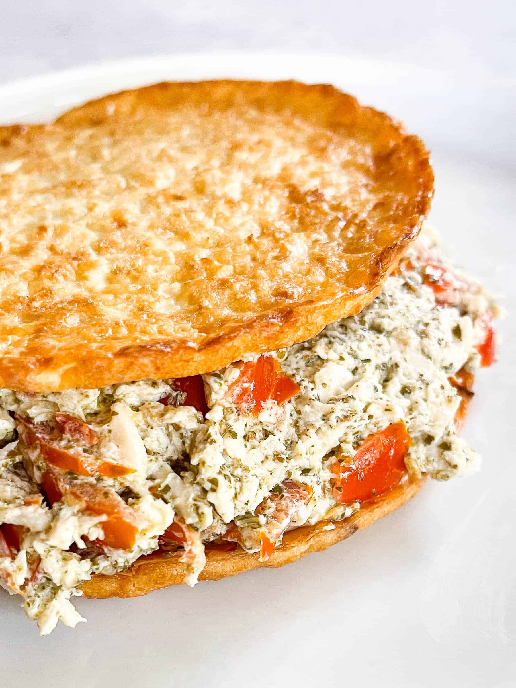 keto pesto chicken salad on cauliflower thins on a white plate with a white background