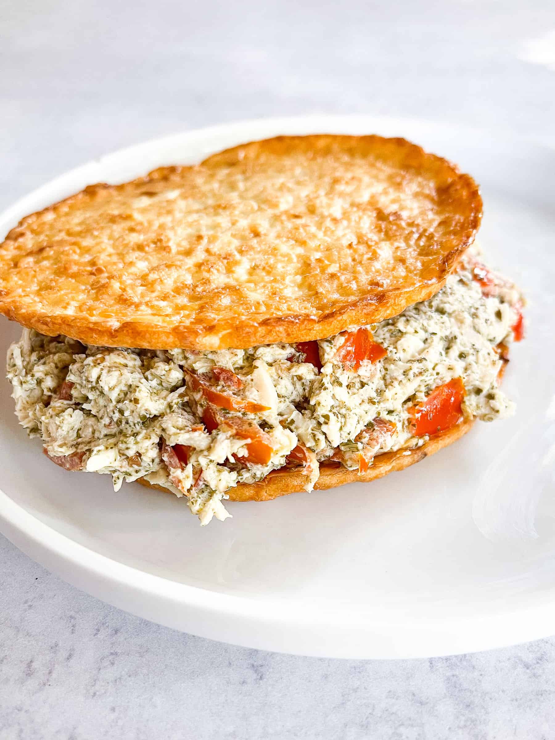 keto pesto chicken salad on cauliflower thins on a white plate with a white background