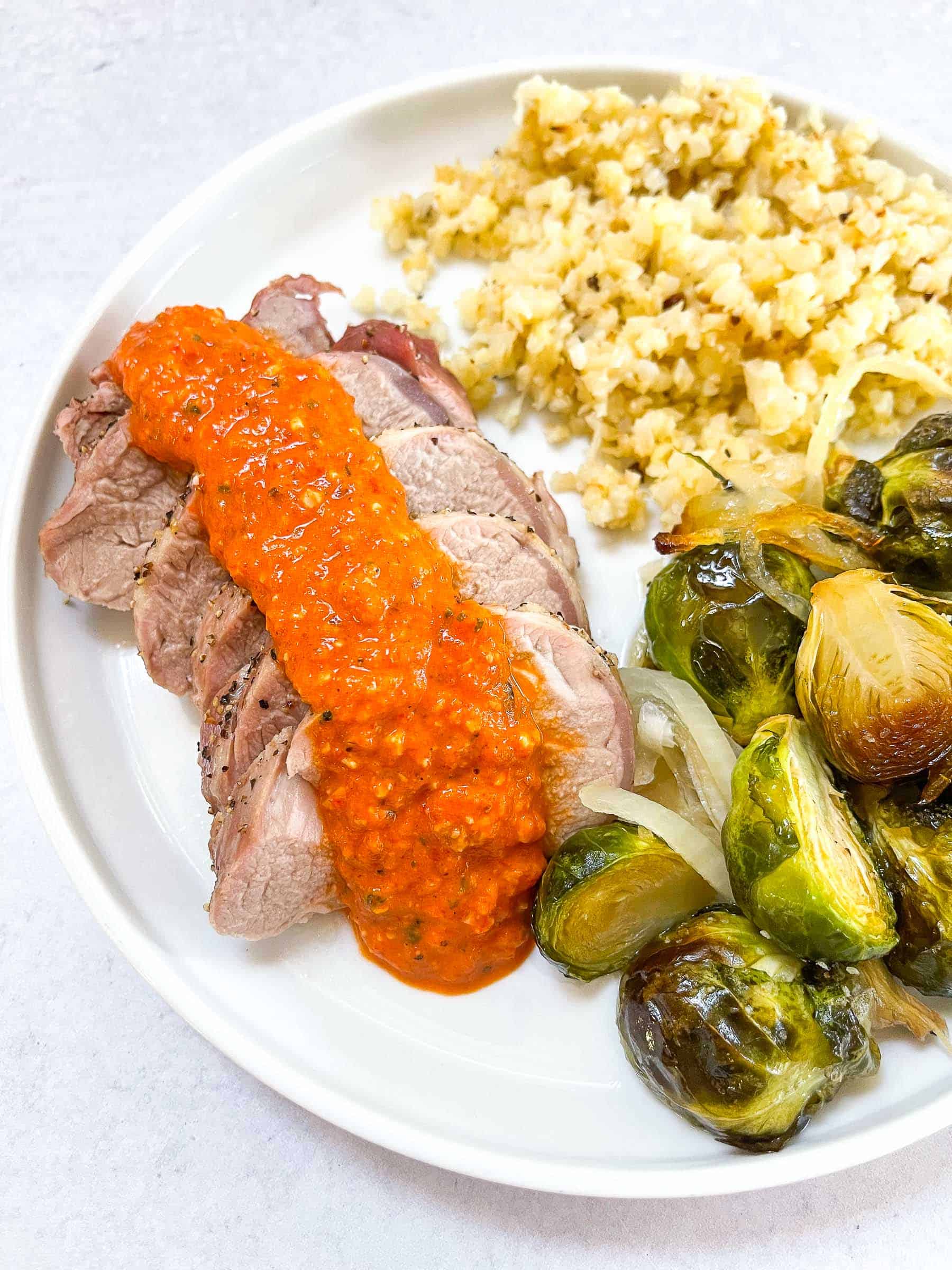 keto sheet pan pork tenderloin with romesco on a white plate with Brussel sprouts and cauliflower rice with a white background