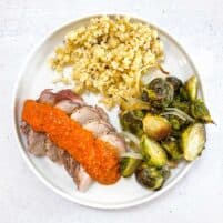 keto sheet pan pork tenderloin with romesco on a white plate with Brussel sprouts and hearts of palm rice with a white background