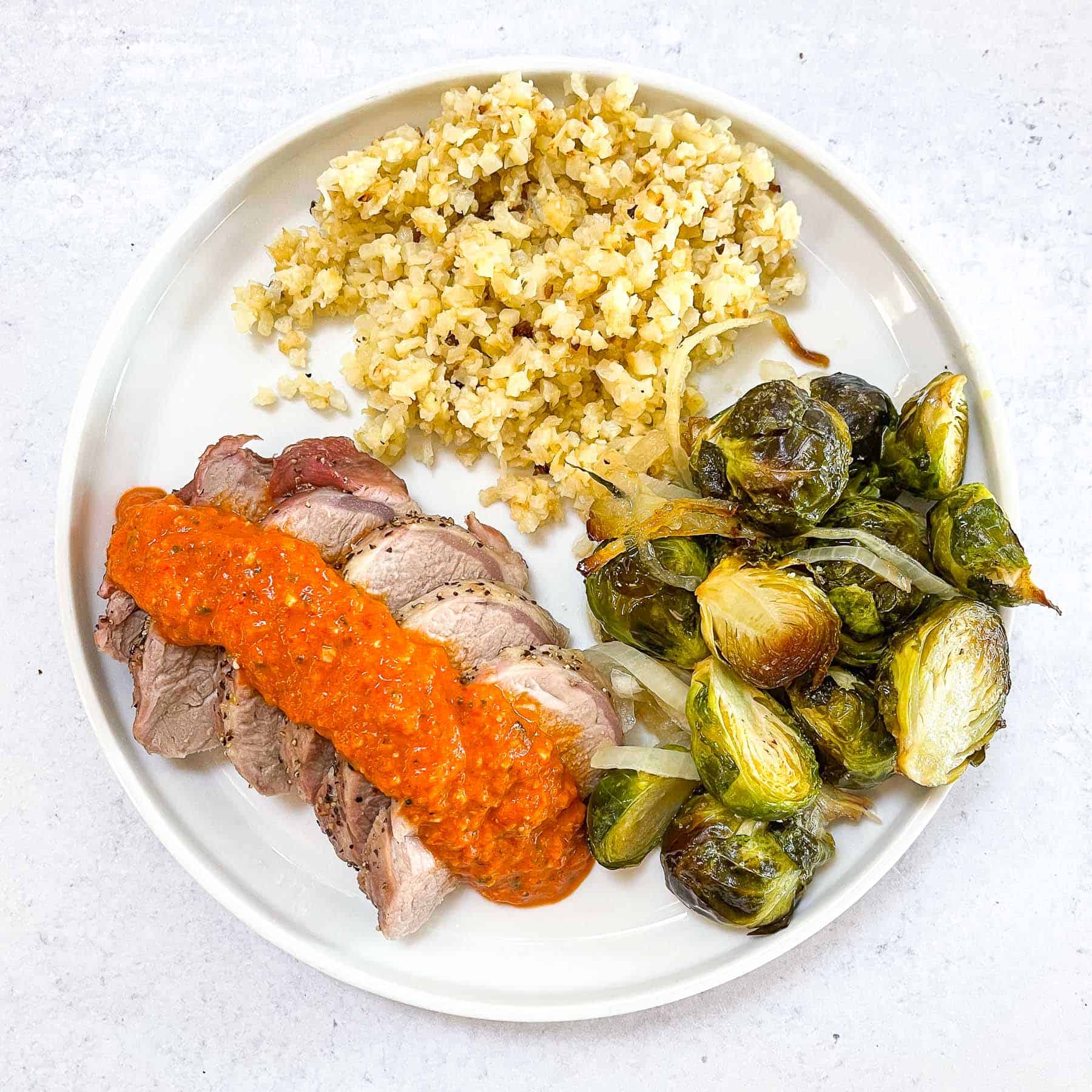 keto sheet pan pork tenderloin with romesco on a white plate with Brussel sprouts and cauliflower rice with a white background