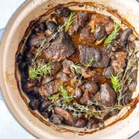 overhead shot of braised beef recipe in a dutch over with fresh herbs as a garnish