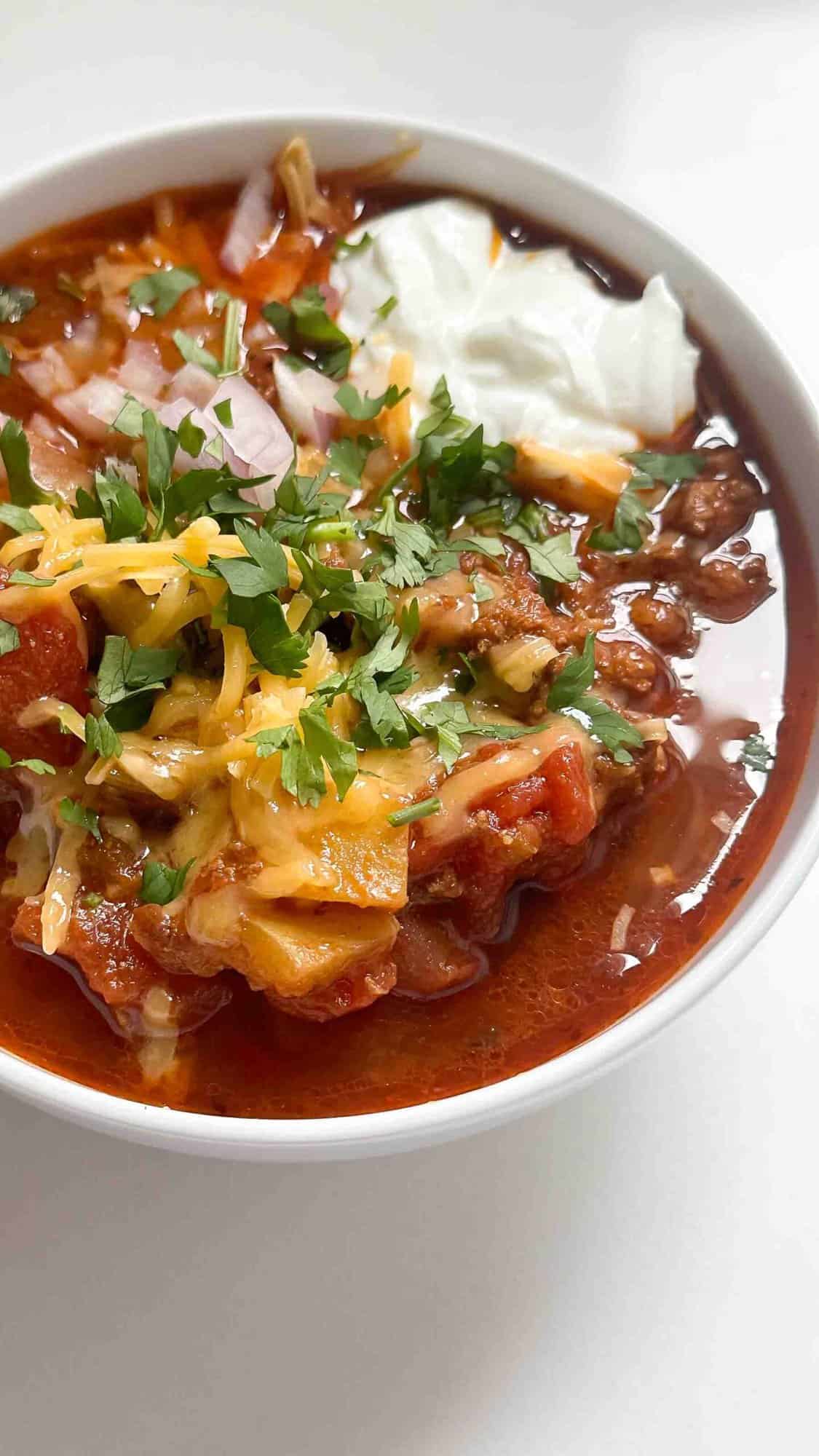 Bowl of Whole30 keto chili garnished with avocado and fresh herbs