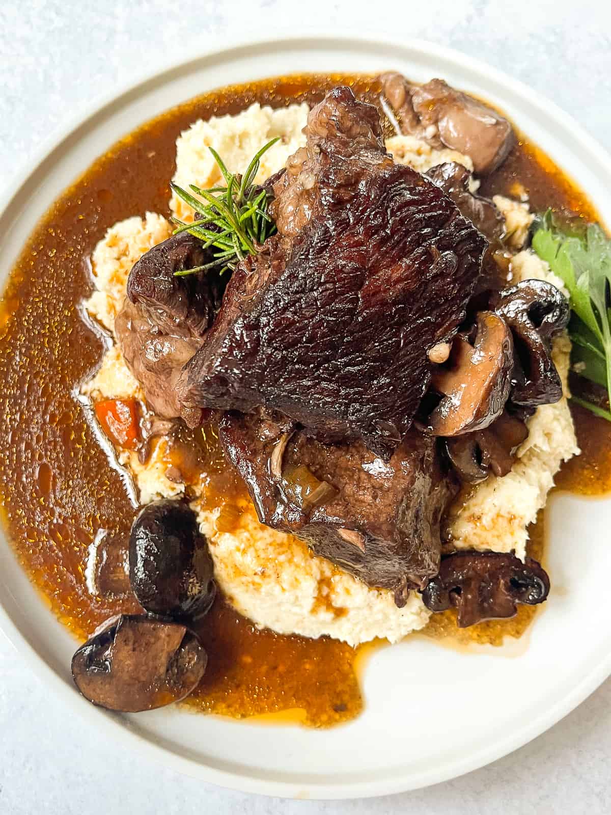 overhead shot of delicious wine braised beef with mushrooms on top of mashed cauliflower on a white plate
