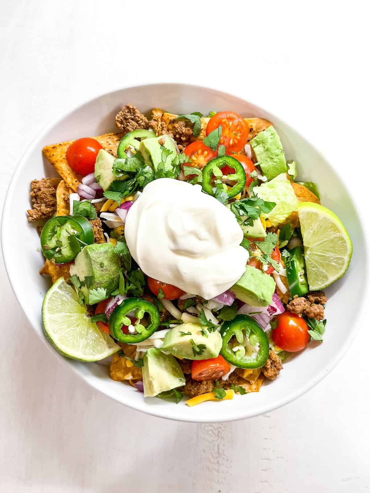 keto taco salad with romaine, ground beef, tomatoes, cheese and sour cream in a white bowl