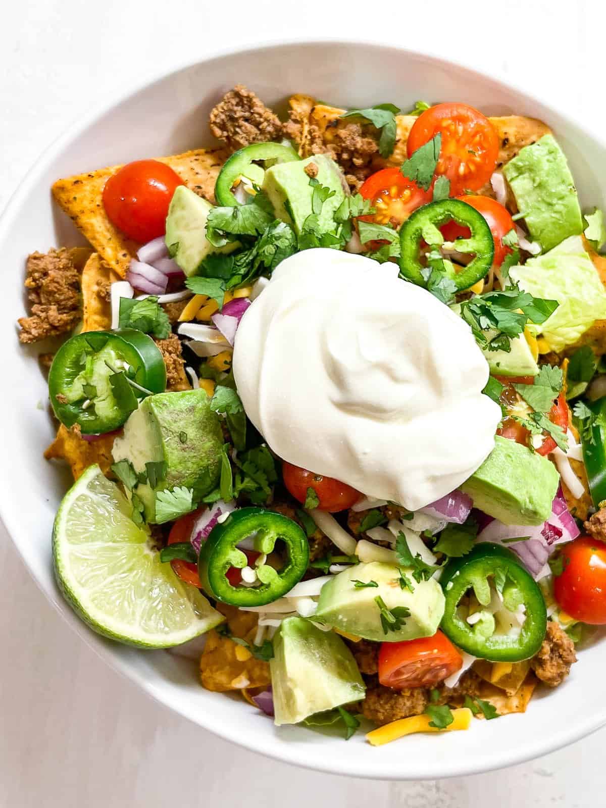 keto taco salad with romaine, ground beef, tomatoes, cheese and sour cream in a white bowl