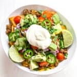 keto taco salad with romaine, ground beef, tomatoes, cheese and sour cream in a white bowl