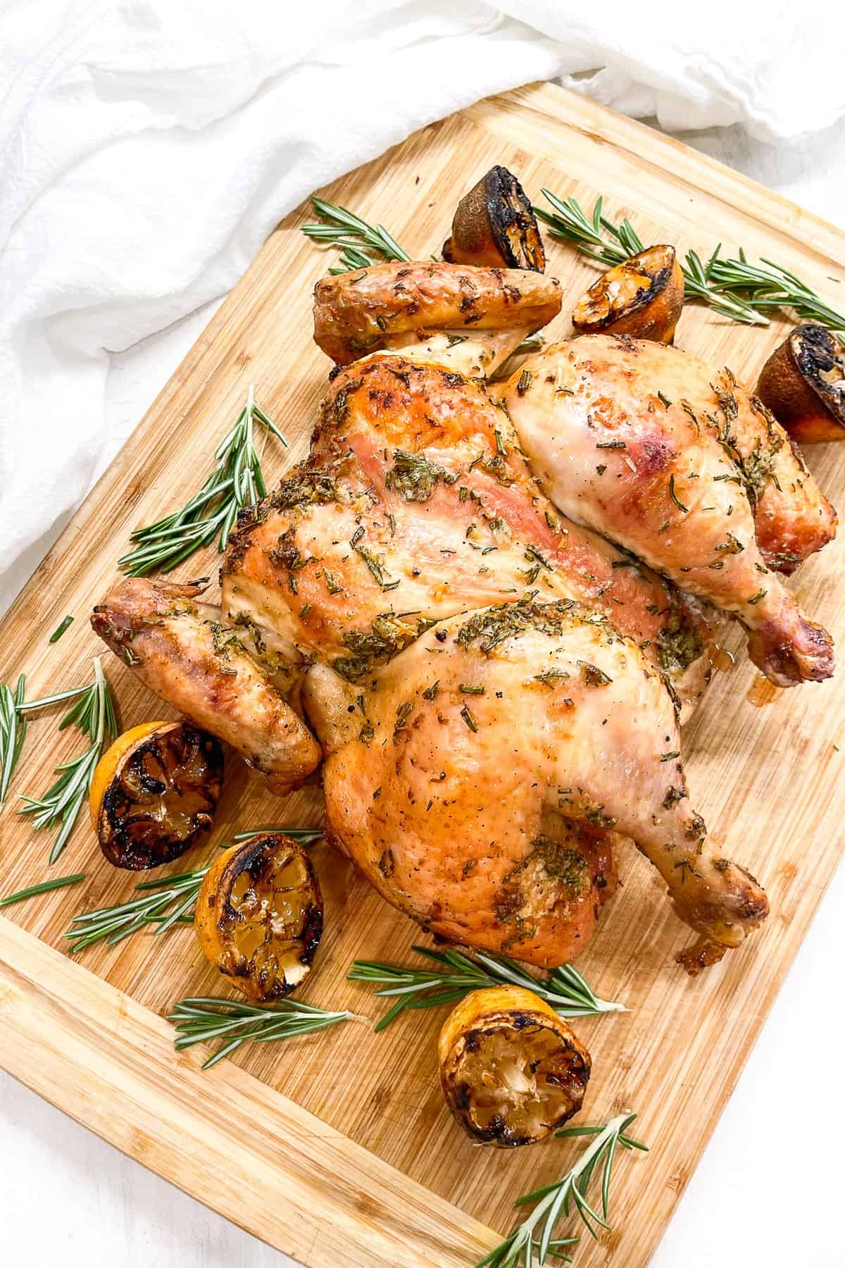 cooked spatchcocked chicken with a rosemary lemon marinade on a cutting board with grilled lemons and fresh rosemary