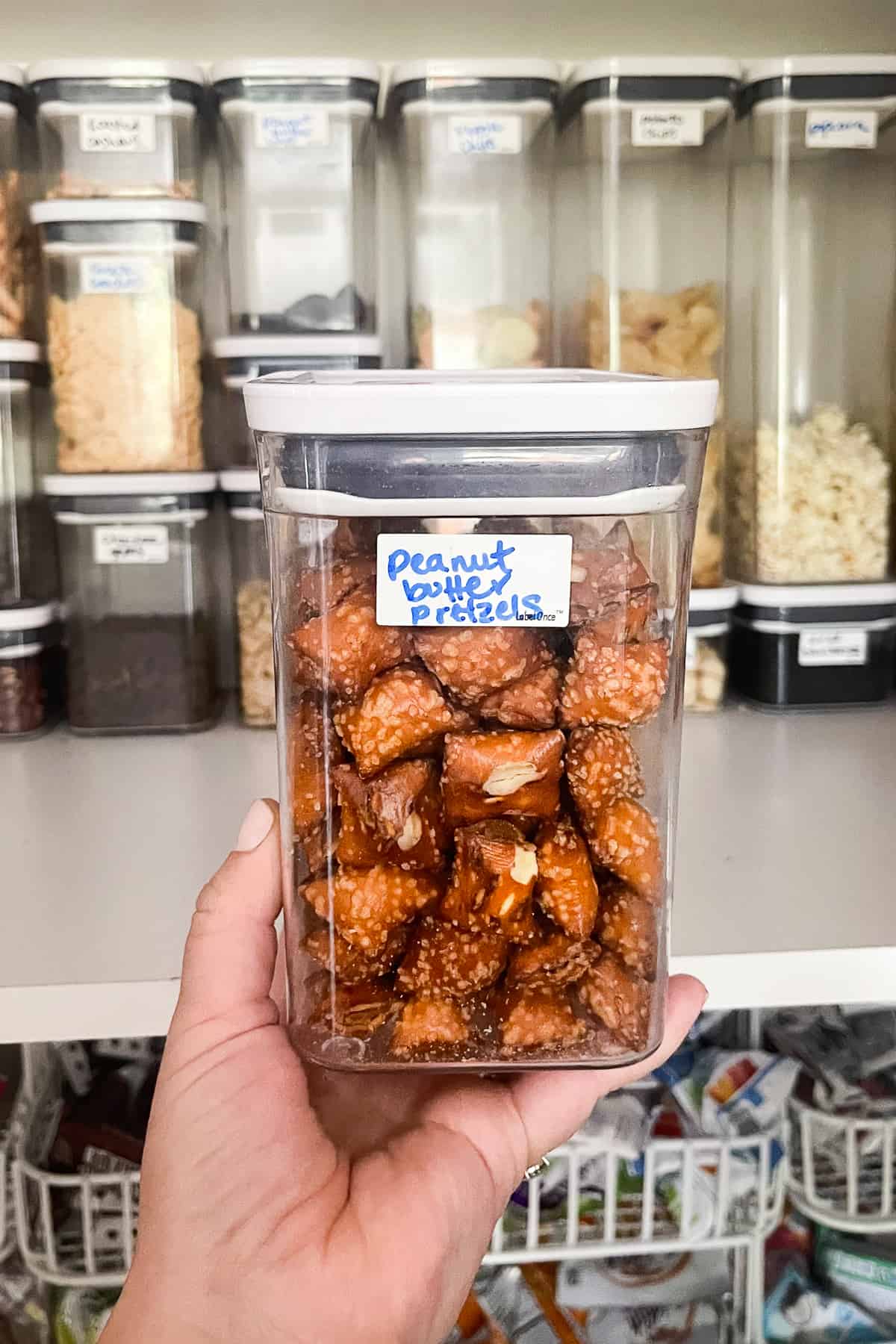 hand holding oxo pop container filled with pretzels with an erasable label with handwriting that says "peanut butter pretzels"