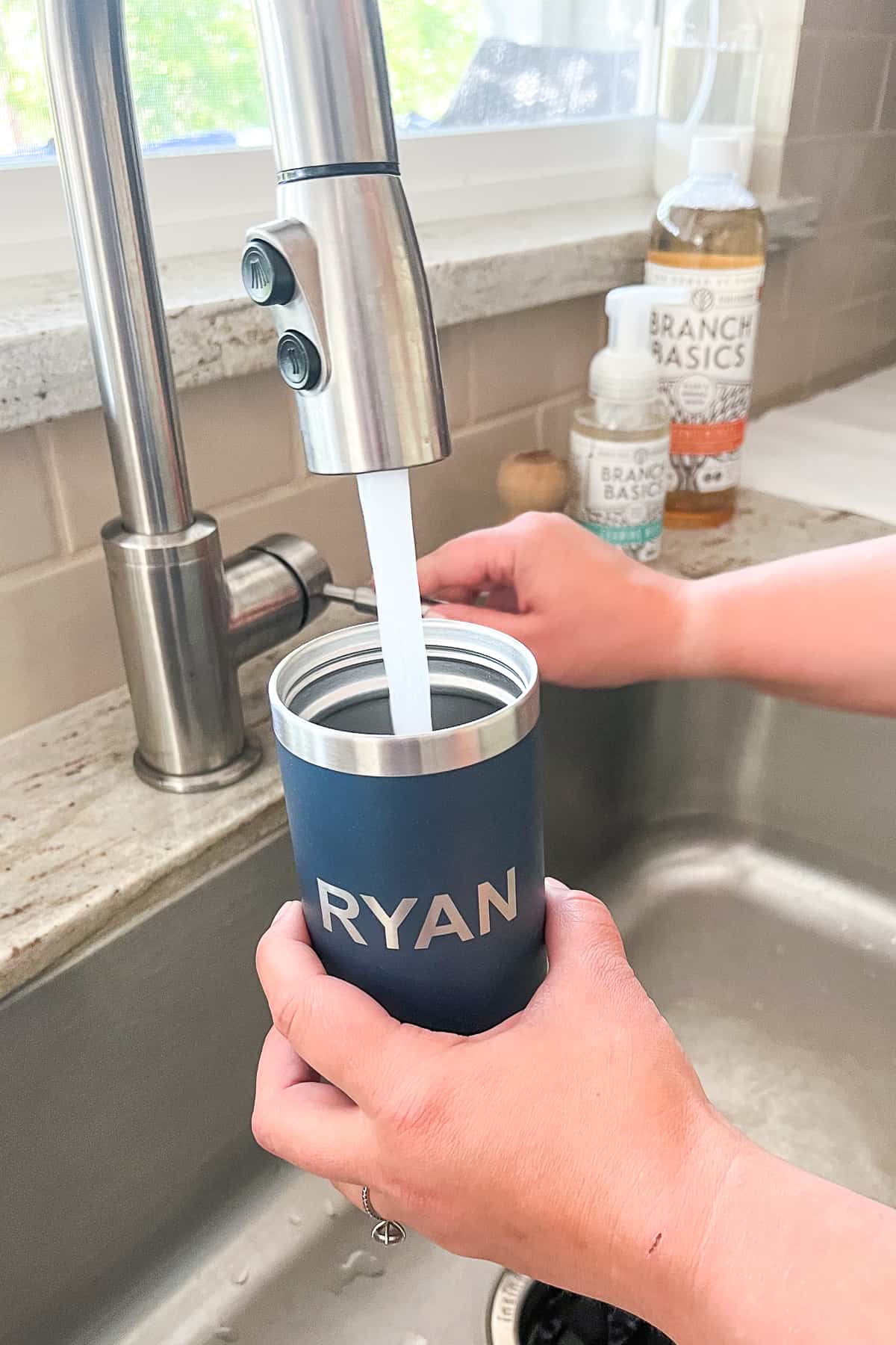 a kitchen sink spout filling up a blue stainless steel tumbler with water