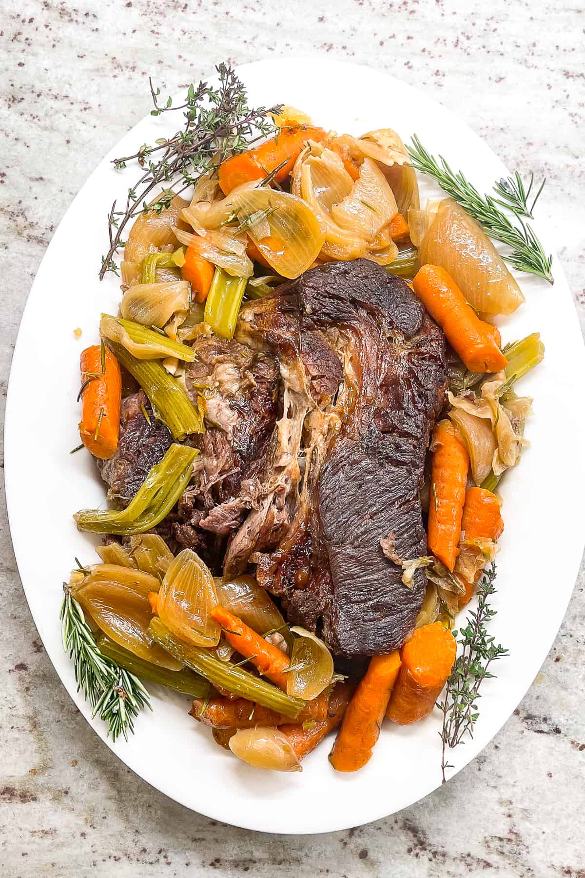 a dutch oven pot roast on a white serving tray with cooked onions, carrots, and celery. 