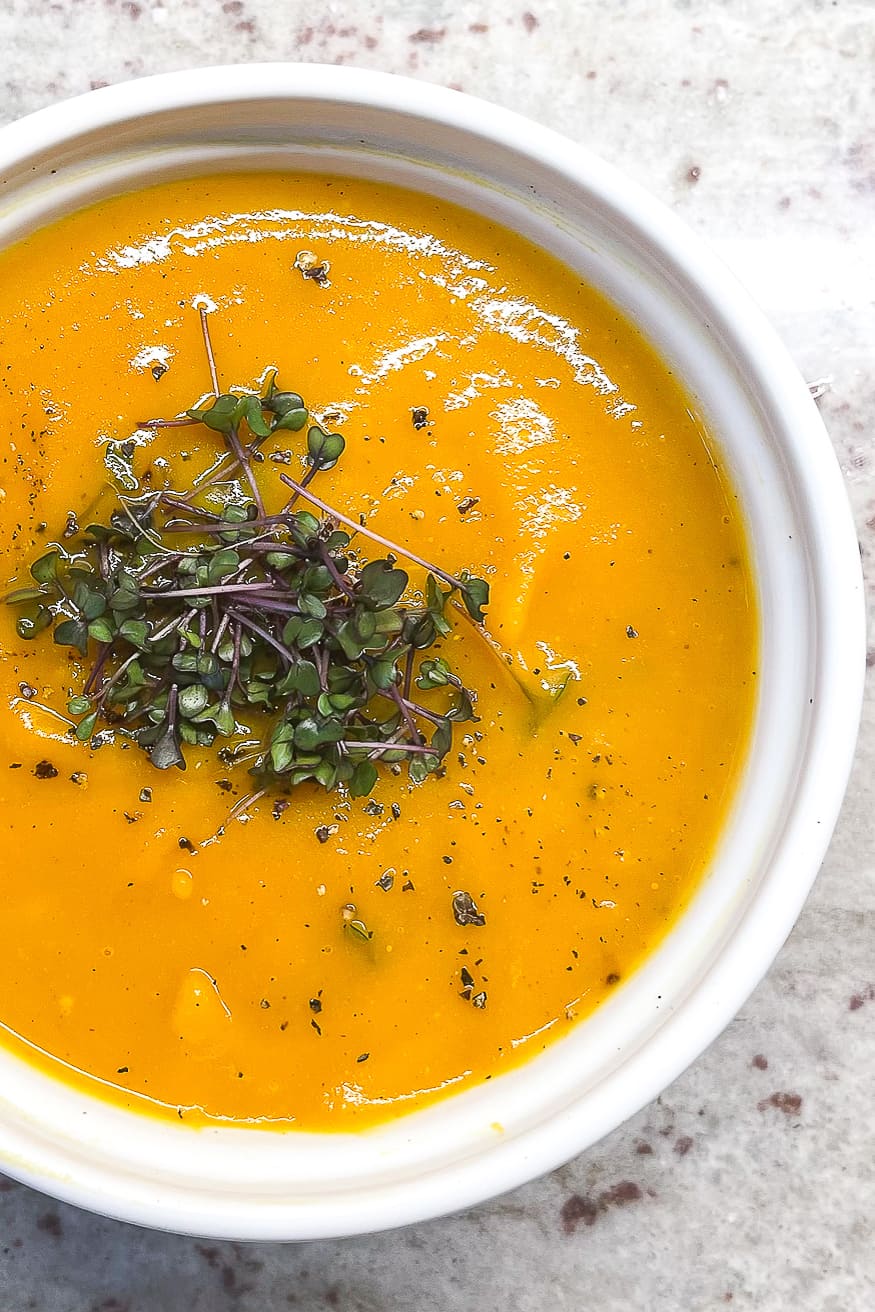 a closeup view of a white bowl filled with soup and topped with microgreens