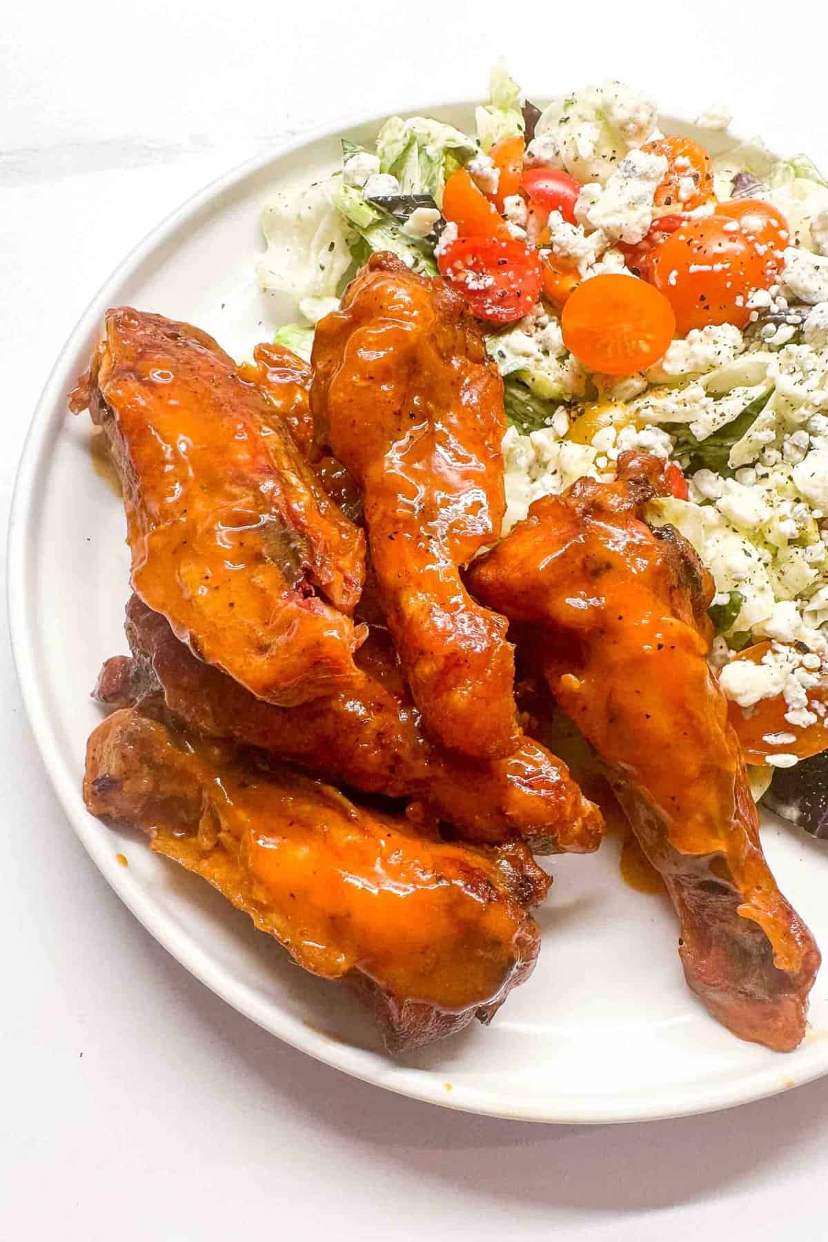 a close up of smoked buffalo wings on a plate with a side salad