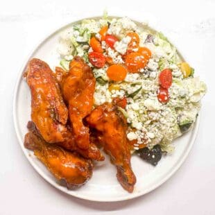 a white plate filled with a salad and buffalo wings