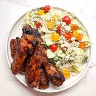 smoked chicken wings on a white plate with a side salad.