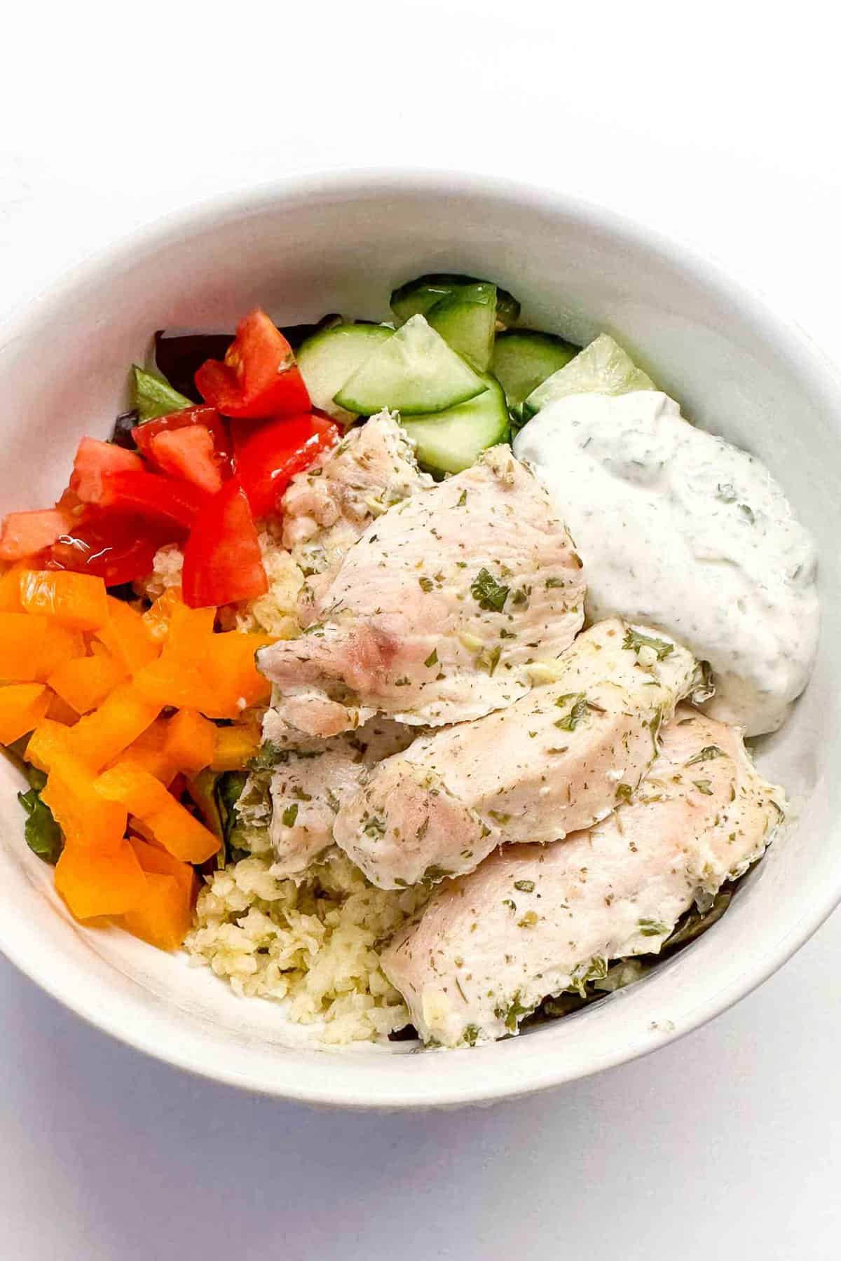 a bowl of greek yogurt chicken in a white bowl with veggies and cauliflower rice