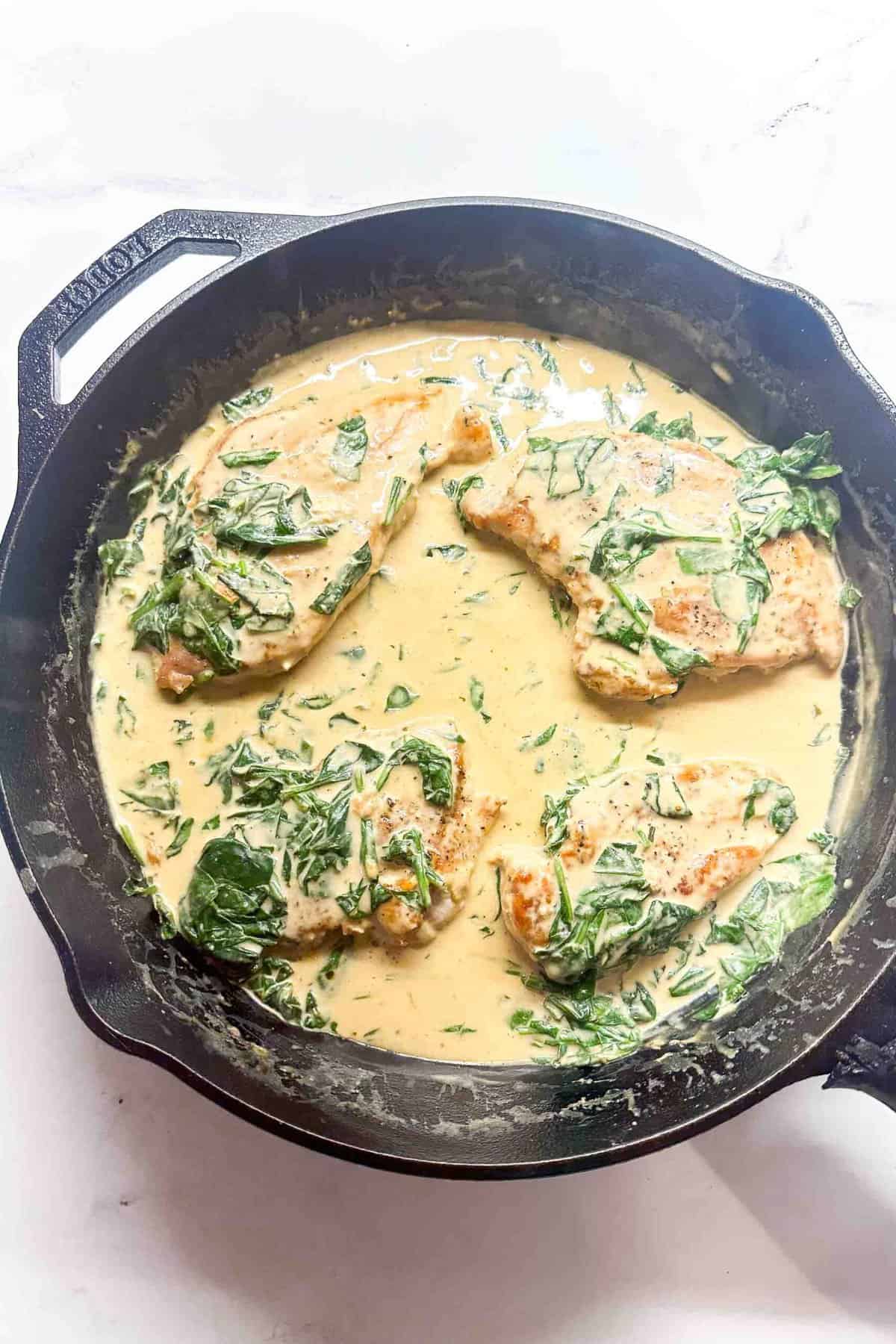 chicken breasts cooking in boursin sauce in a cast iron skillet