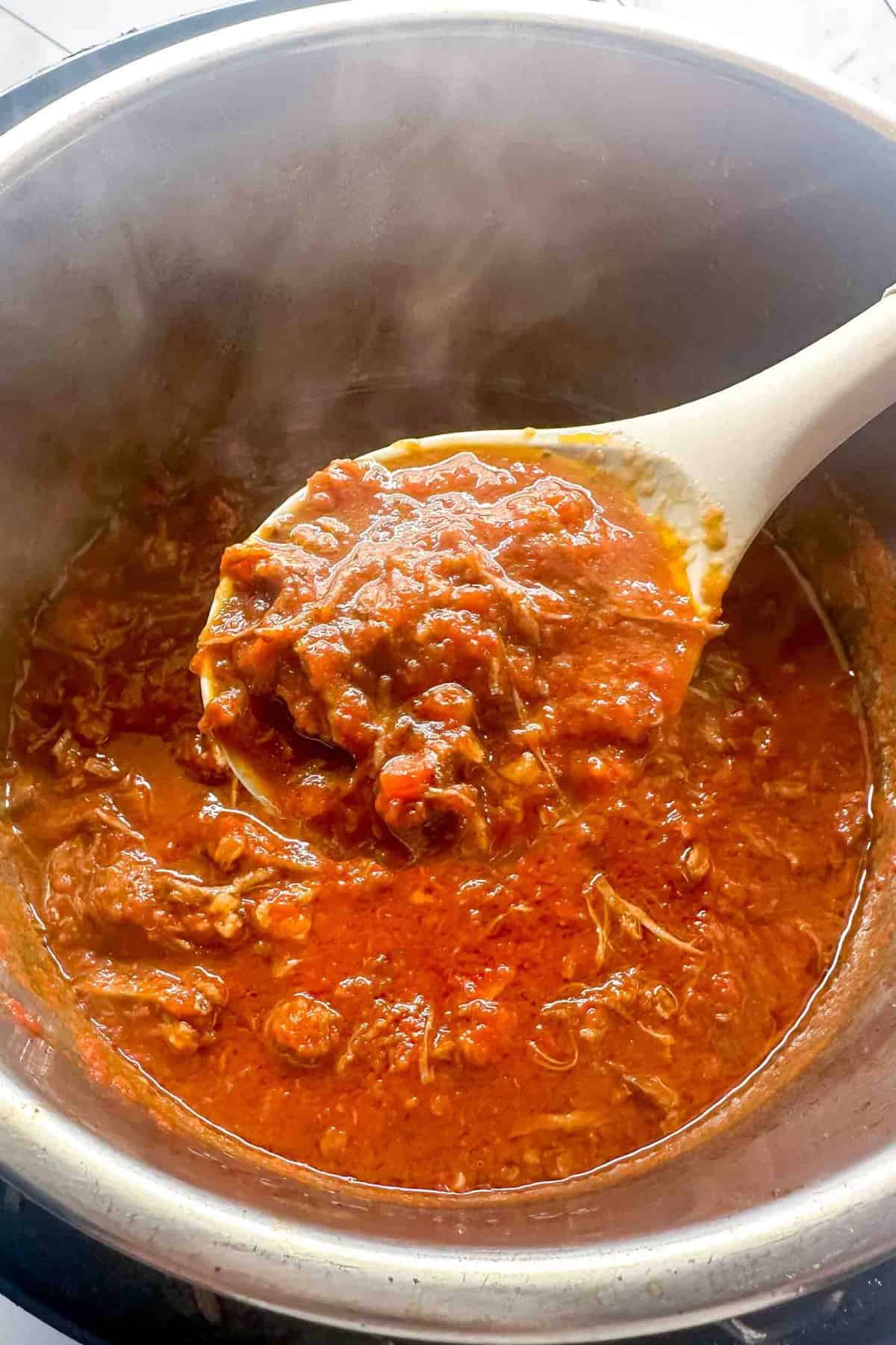 a wooden spoon scooping ragu out of the pot