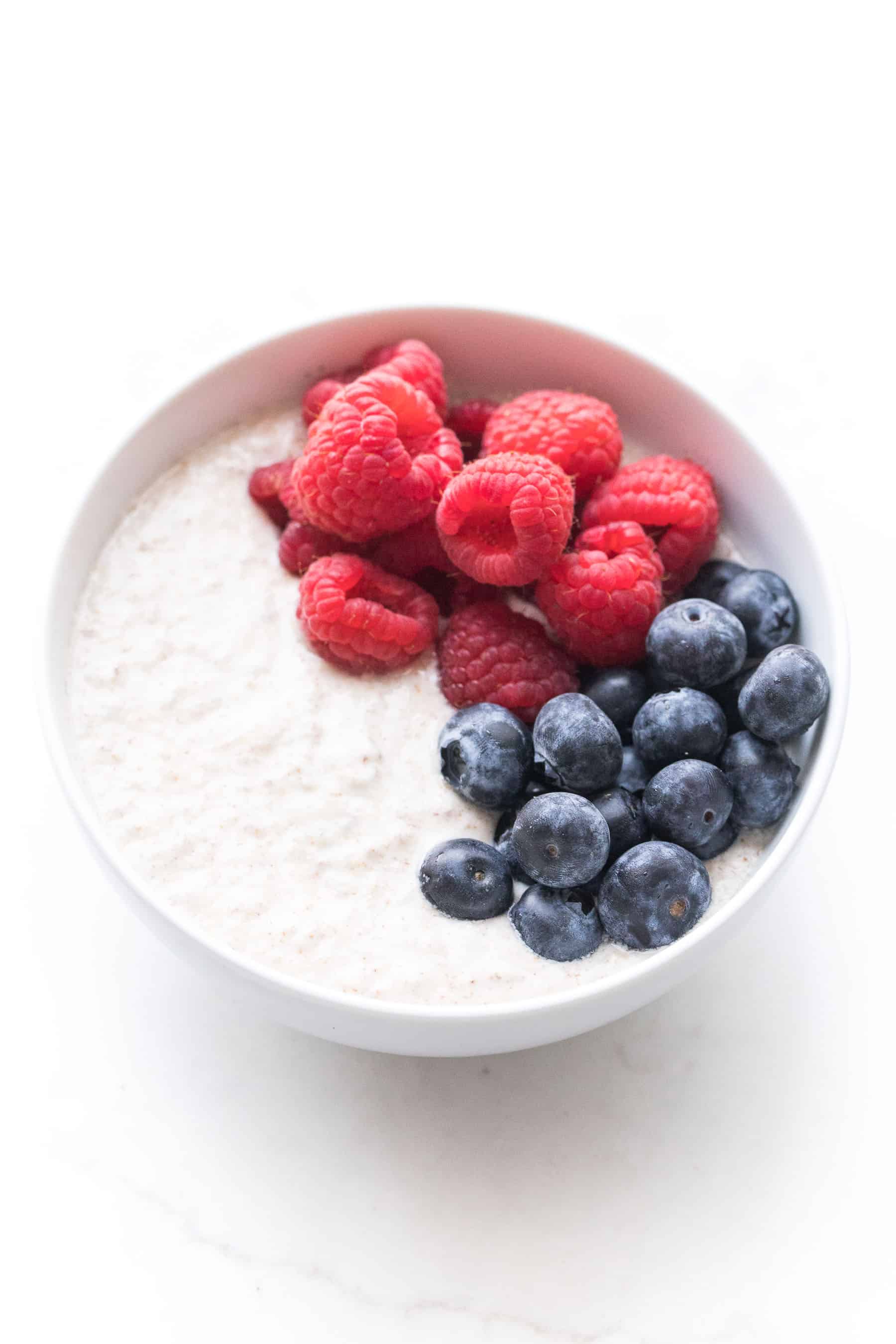 white bowl with breakfast porridge, raspberries and blueberries