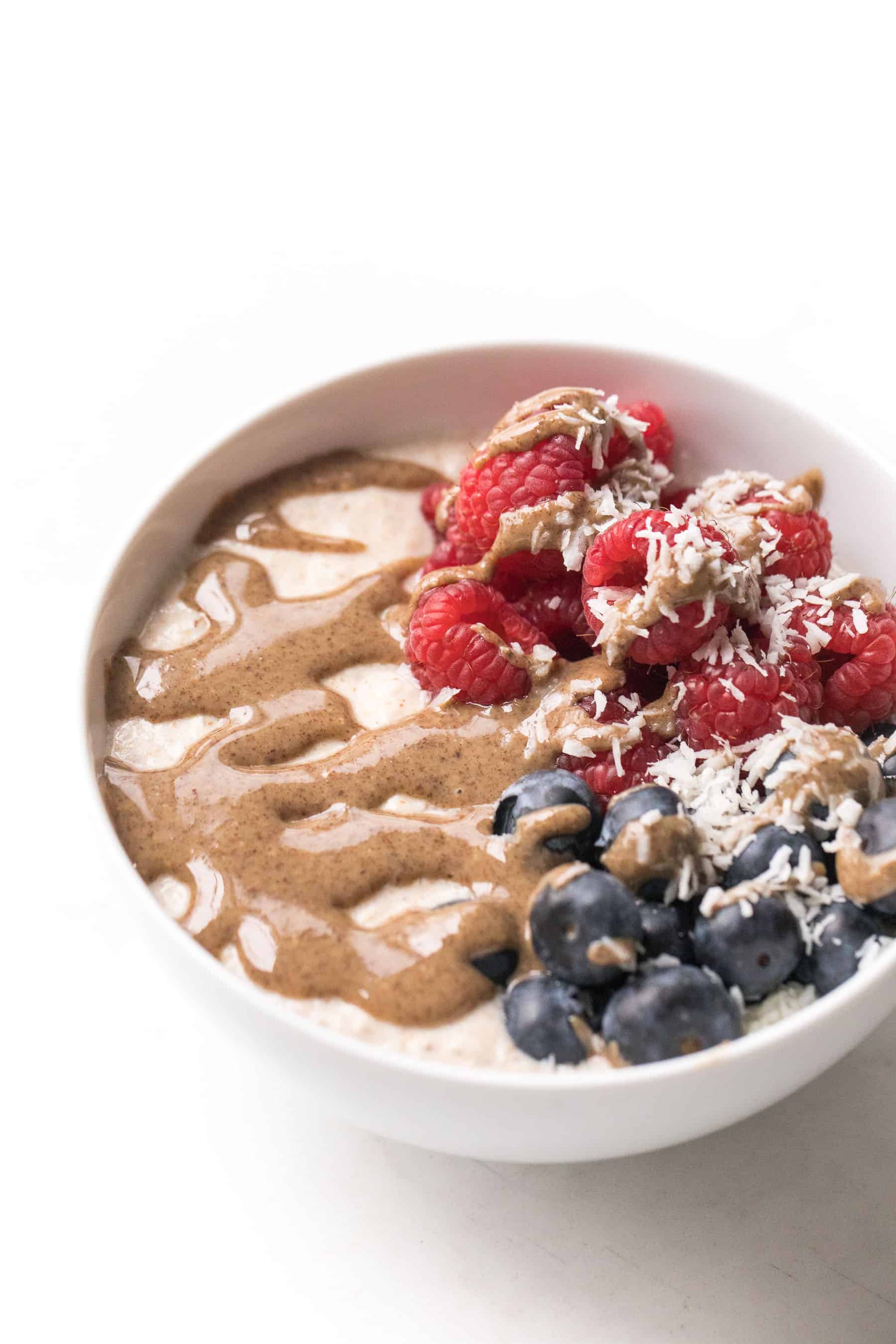 white bowl with breakfast porridge, berries and nut butter