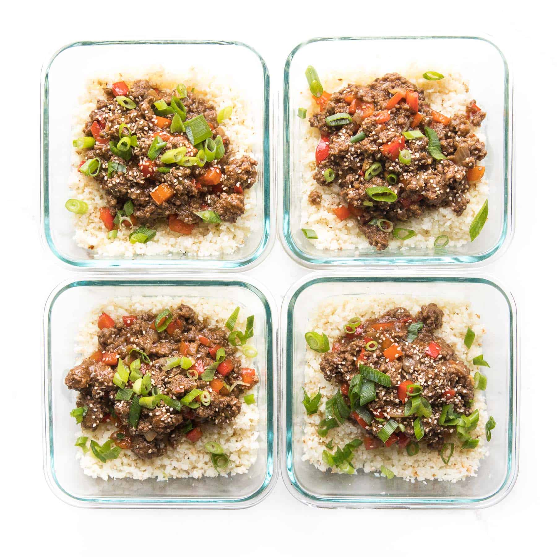 ground asian beef + bell peppers topped with green onions over cauliflower rice in a meal prep container