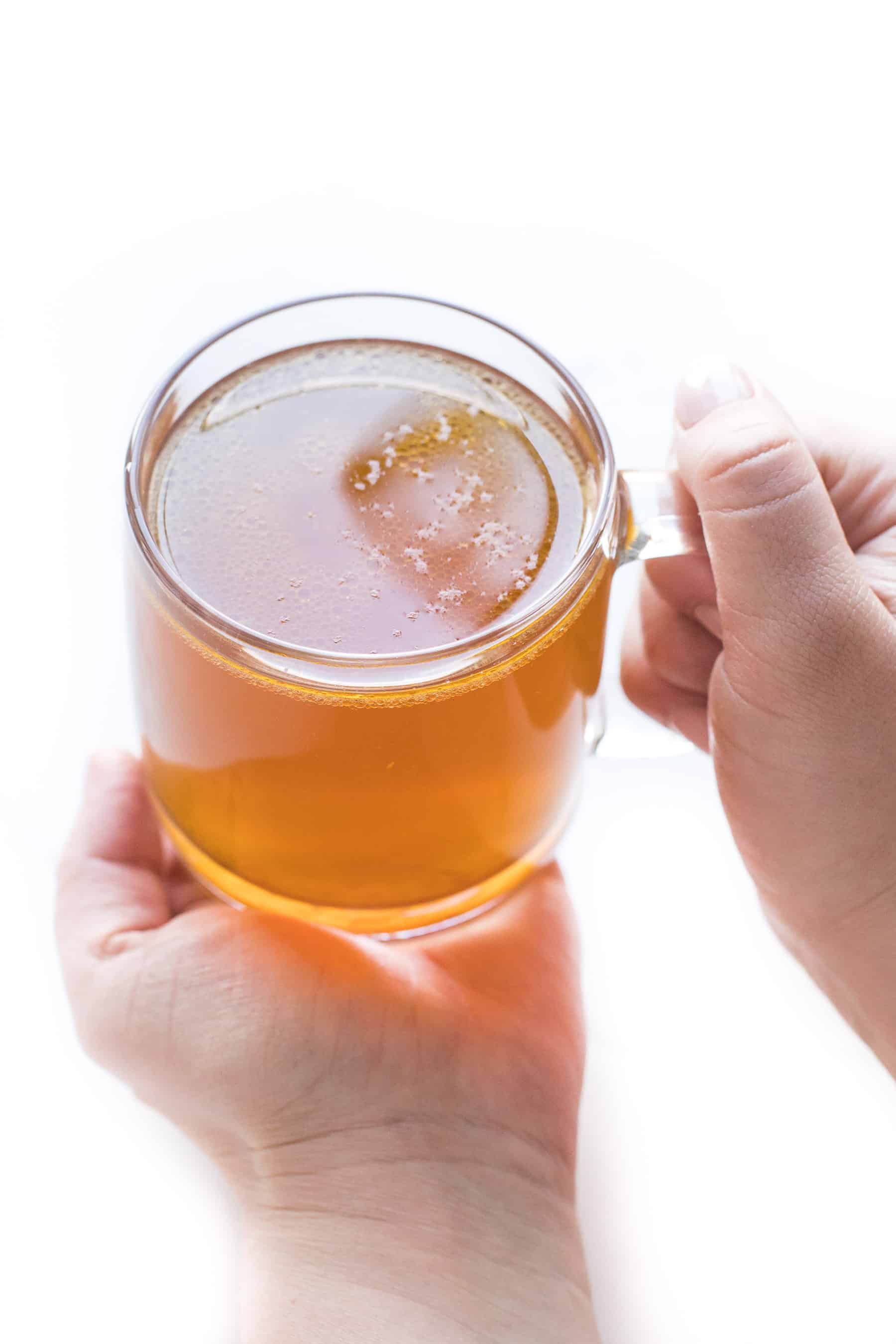 2 hands holding a clear mug of bone broth