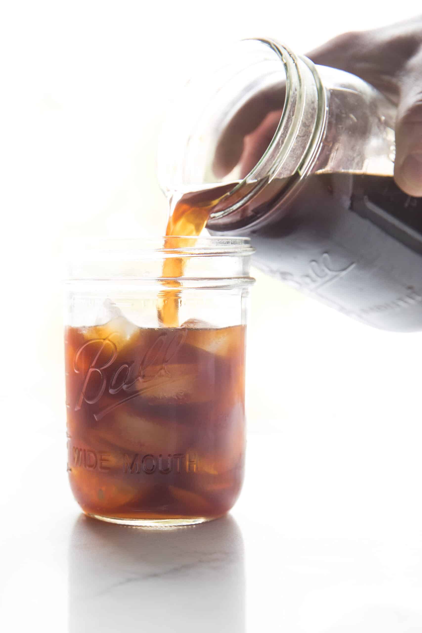 pouring cold brew coffee into a mason jar filled with ice