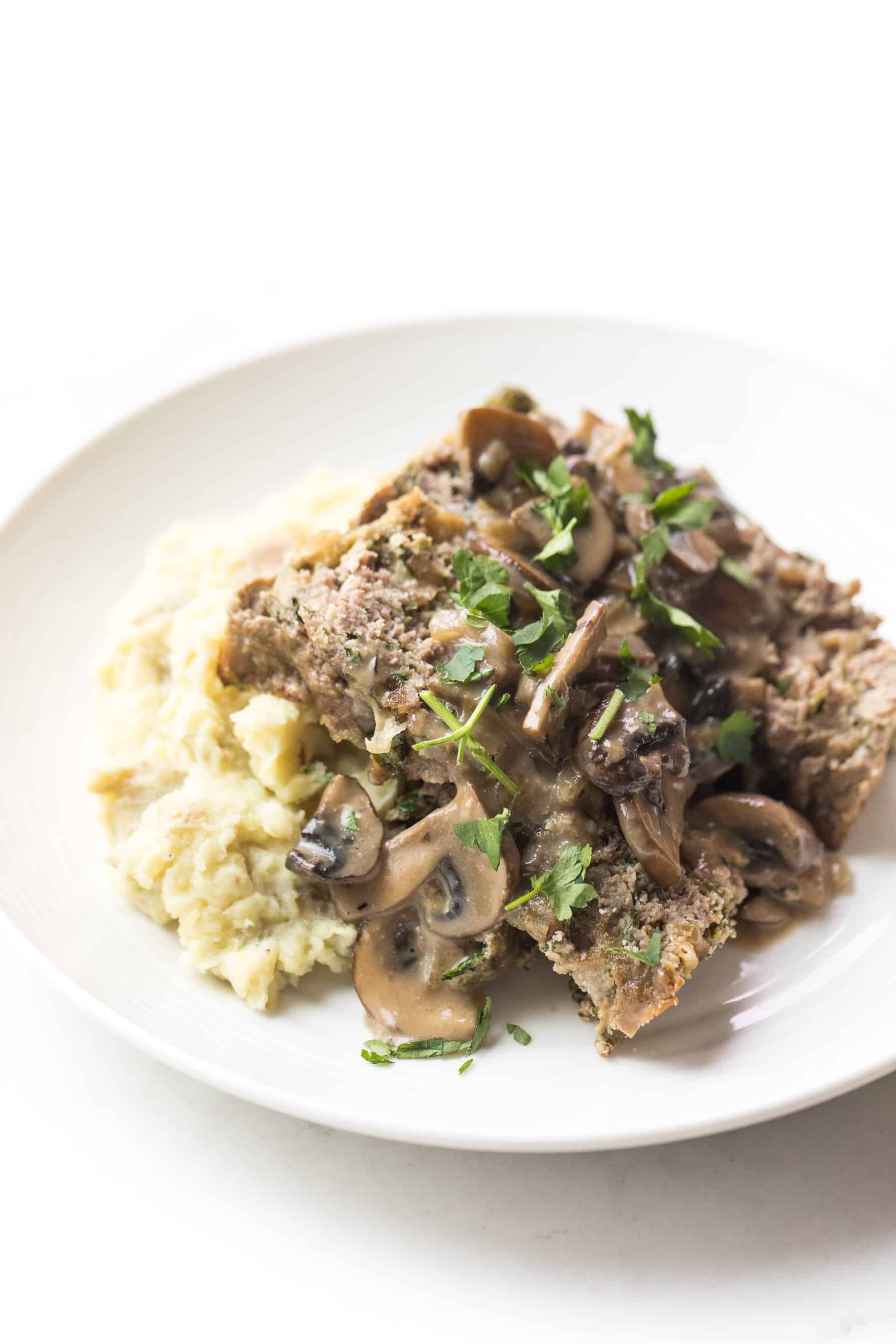 White plate with meatloaf and mushroom gravy over mashed potatoes