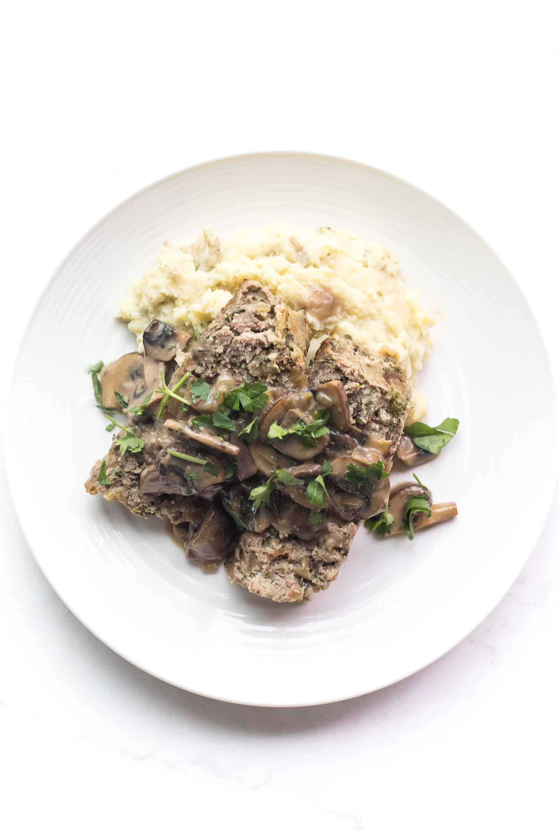 white plate with meatloaf and mushroom gravy over mashed potatoes