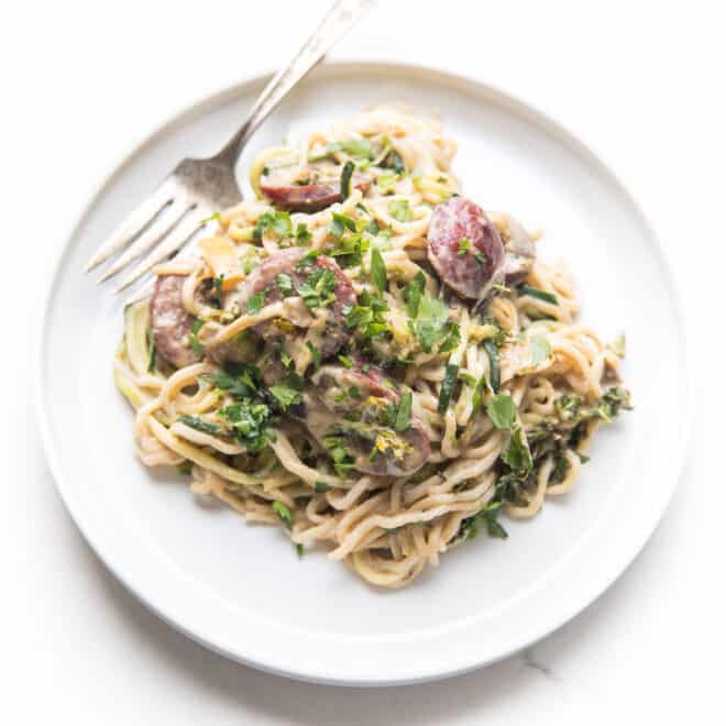 creamy cajun sausage pasta on a white plate with a silver fork resting on the side