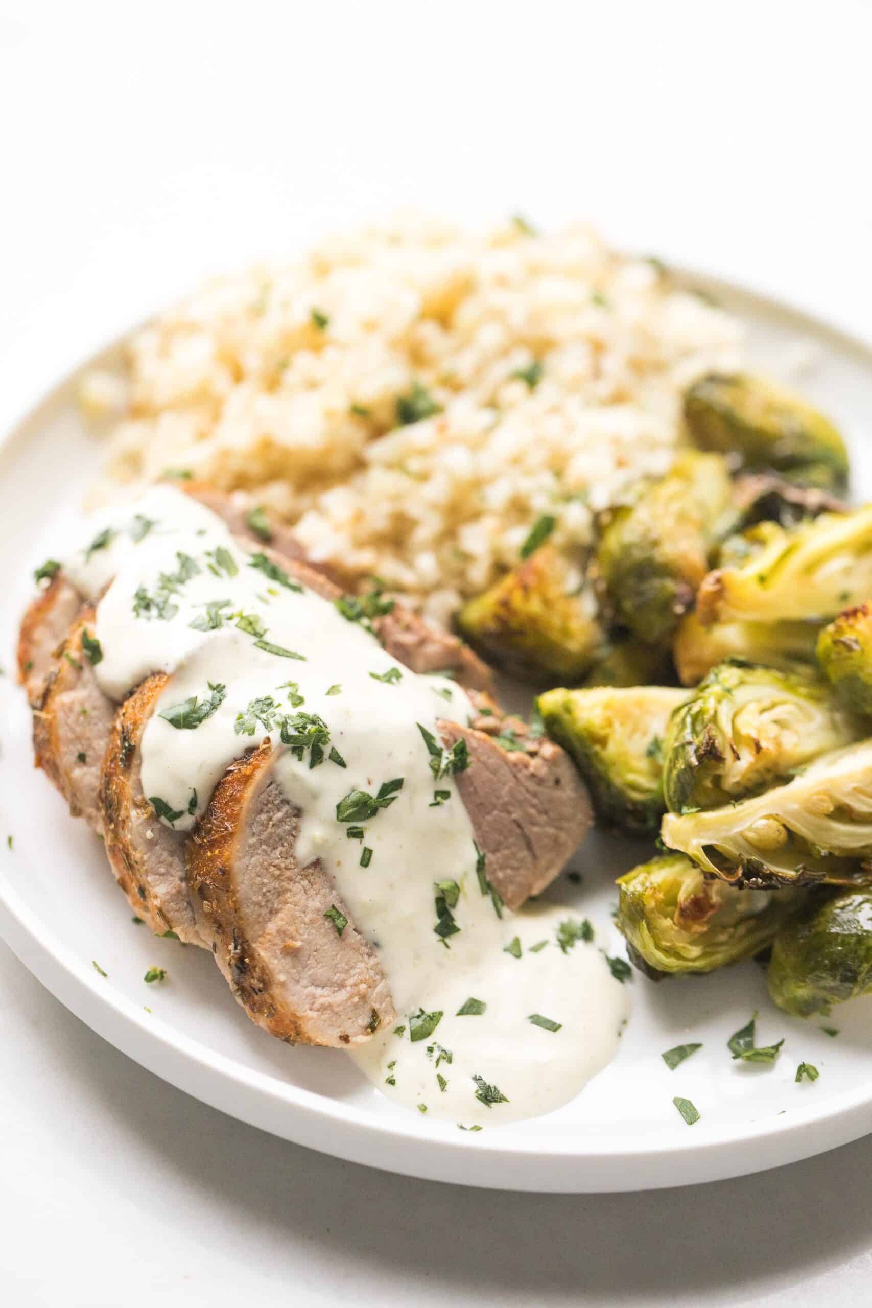 blackened pork tenderloin topped with white sauce lime garlic aioli with with brussels sprouts and cauliflower rice